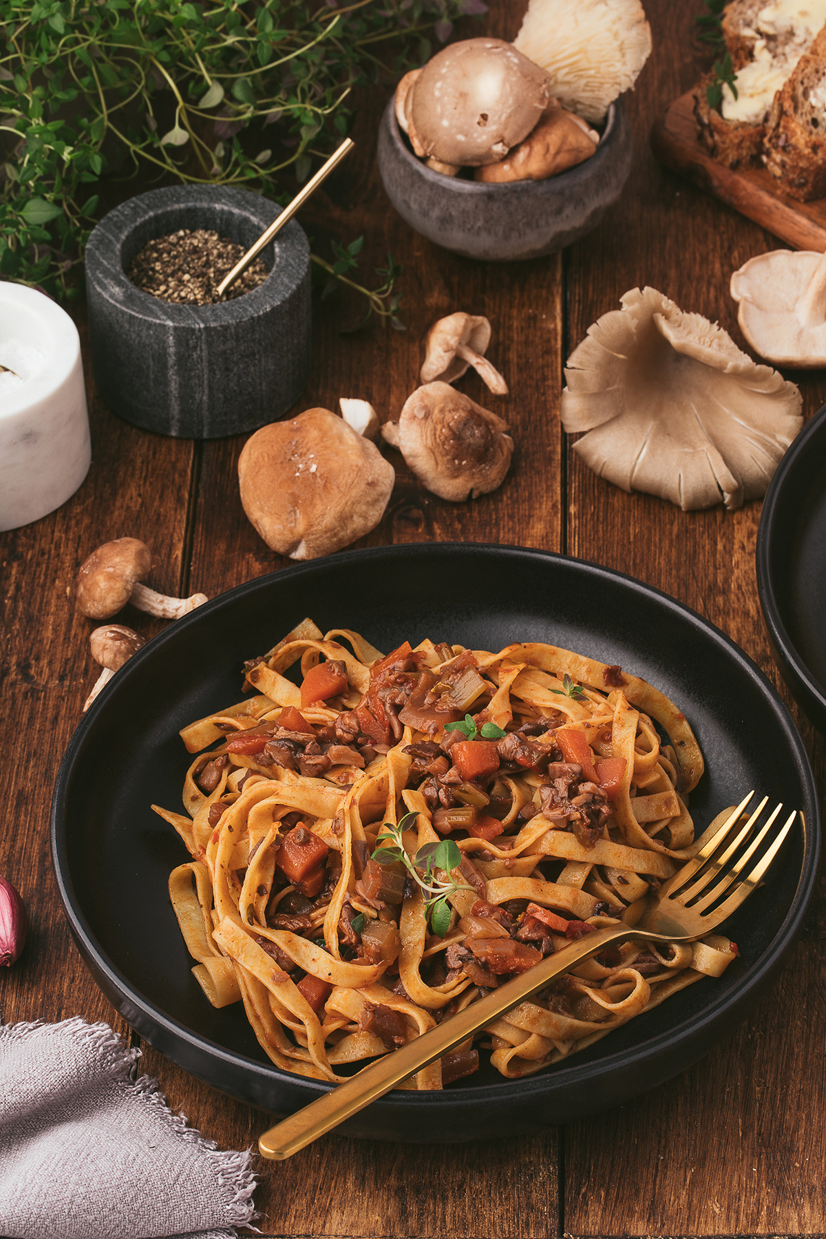 Tagliatelle pasta with a rich mushroom ragu in a black bowl on a wooden table, surrounded by fresh mushrooms and herbs—perfect for those seeking the best ragu recipe or a flavorful vegan pasta sauce option.