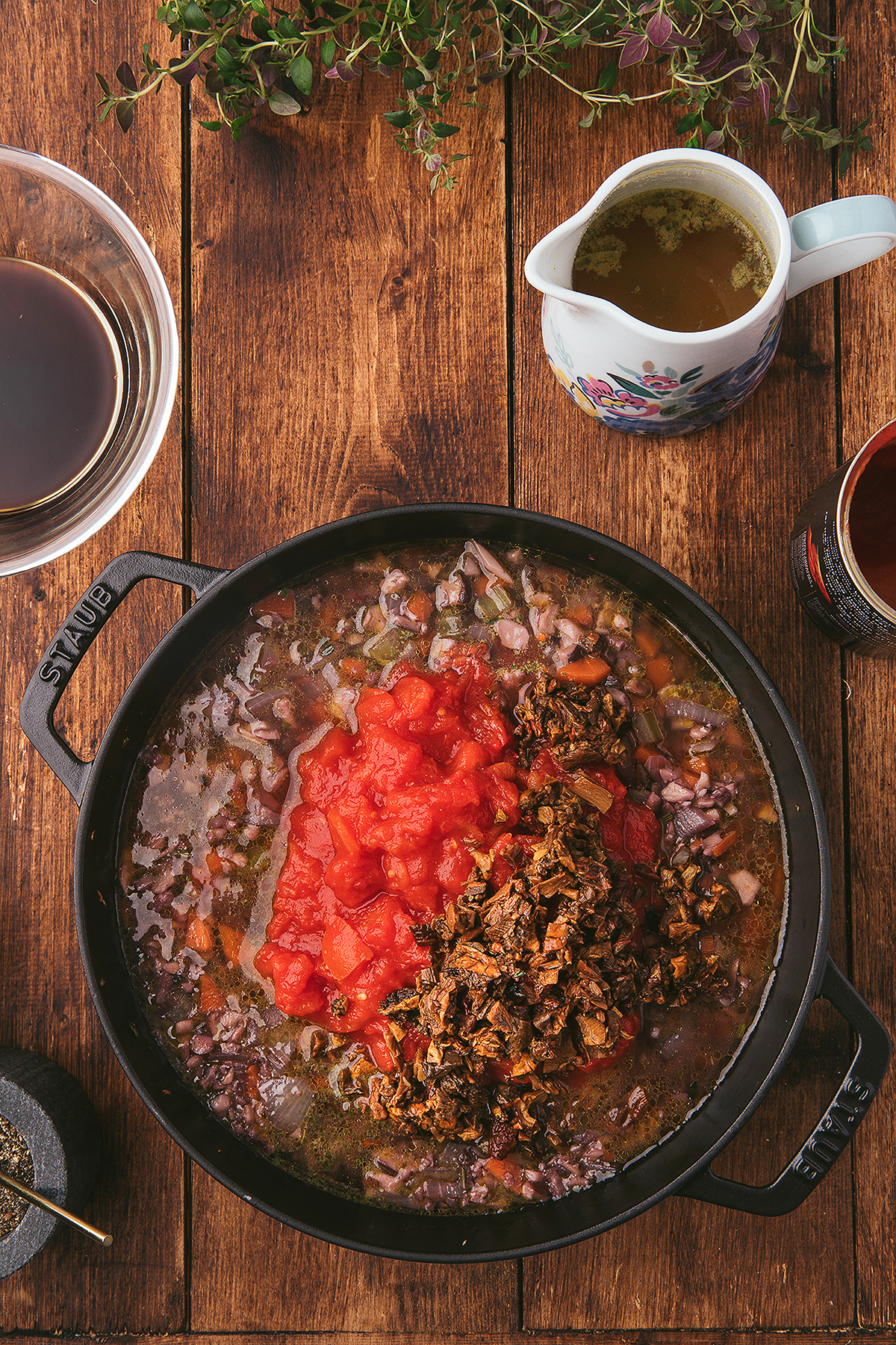 A black pot of meatless ragu with tomatoes and vegetables sits on a wooden table, surrounded by bowls and a jug—a homemade spaghetti sauce with mushrooms ready to serve.