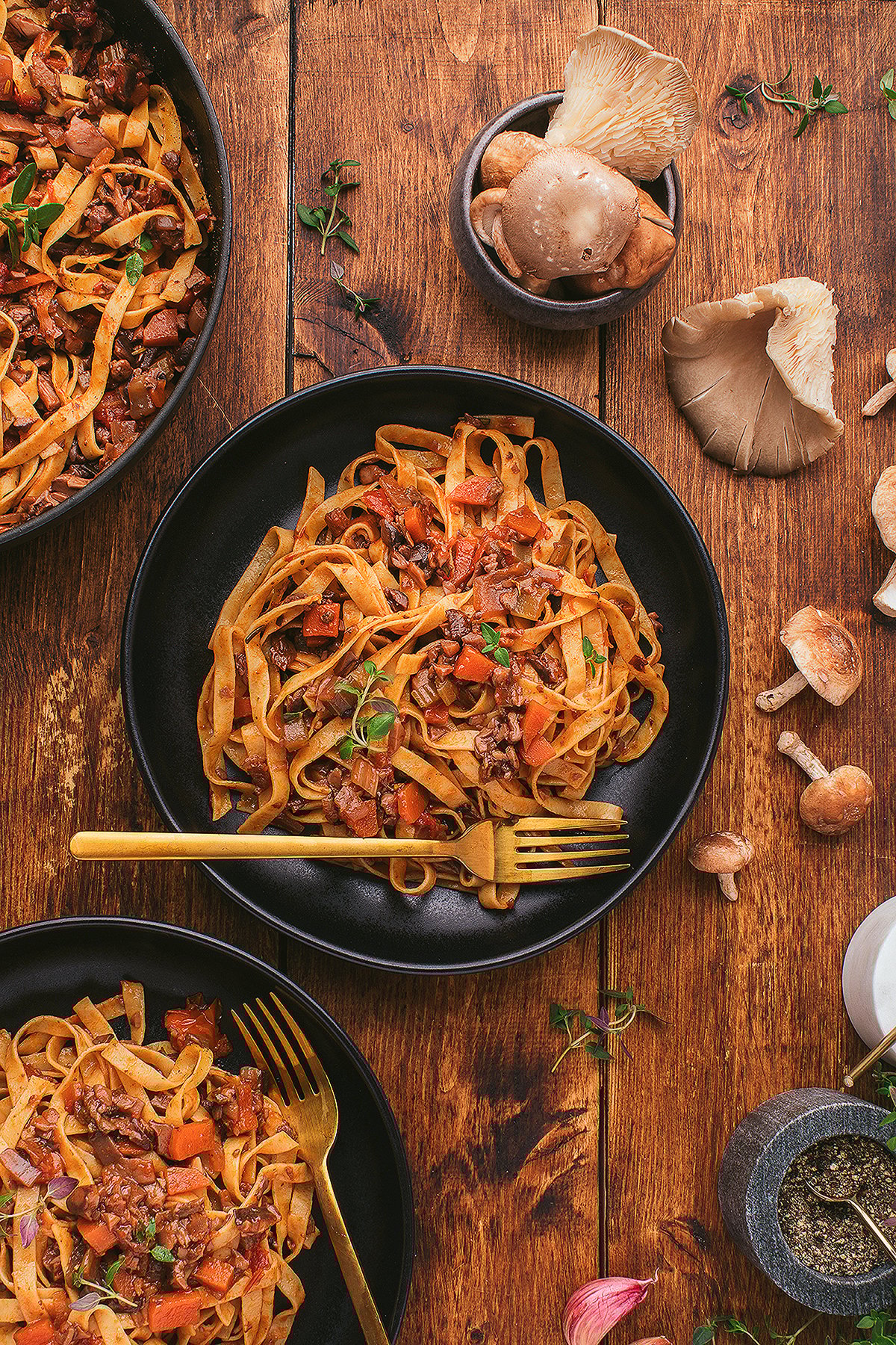 Tagliatelle pasta with a savory meatless ragu of mushrooms and vegetables in black bowls on a wooden table, garnished with herbs.