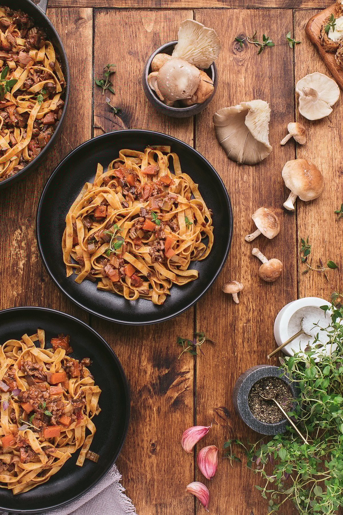 Overhead view of pasta with tomato and mushrooms on black plates, surrounded by fresh mushrooms and herbs—perfect for showcasing the best ragu recipe or a homemade spaghetti sauce with mushrooms.