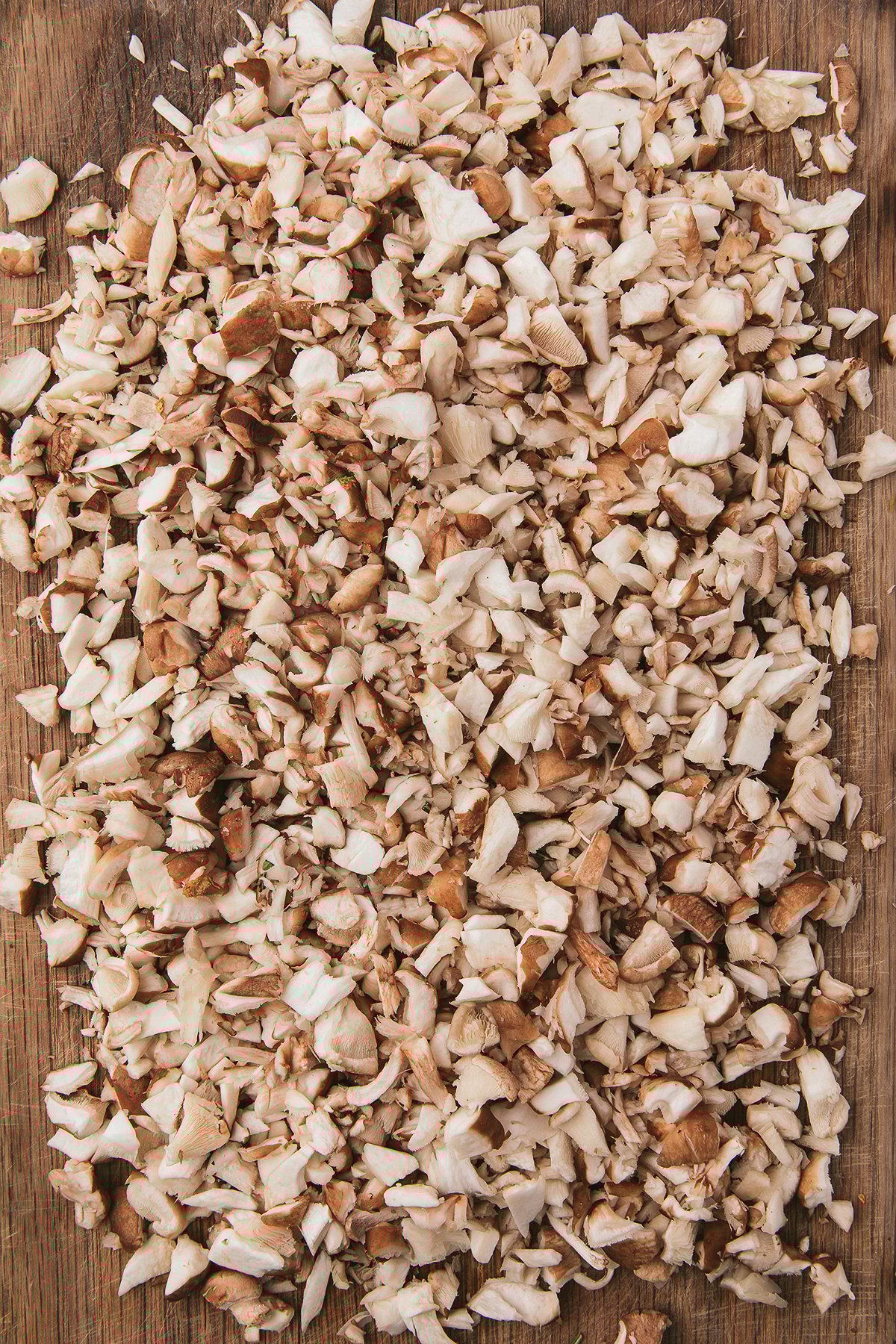 Finely chopped mushrooms spread out on a wooden cutting board, ready to be transformed into a rich vegan pasta sauce or hearty mushroom ragu.