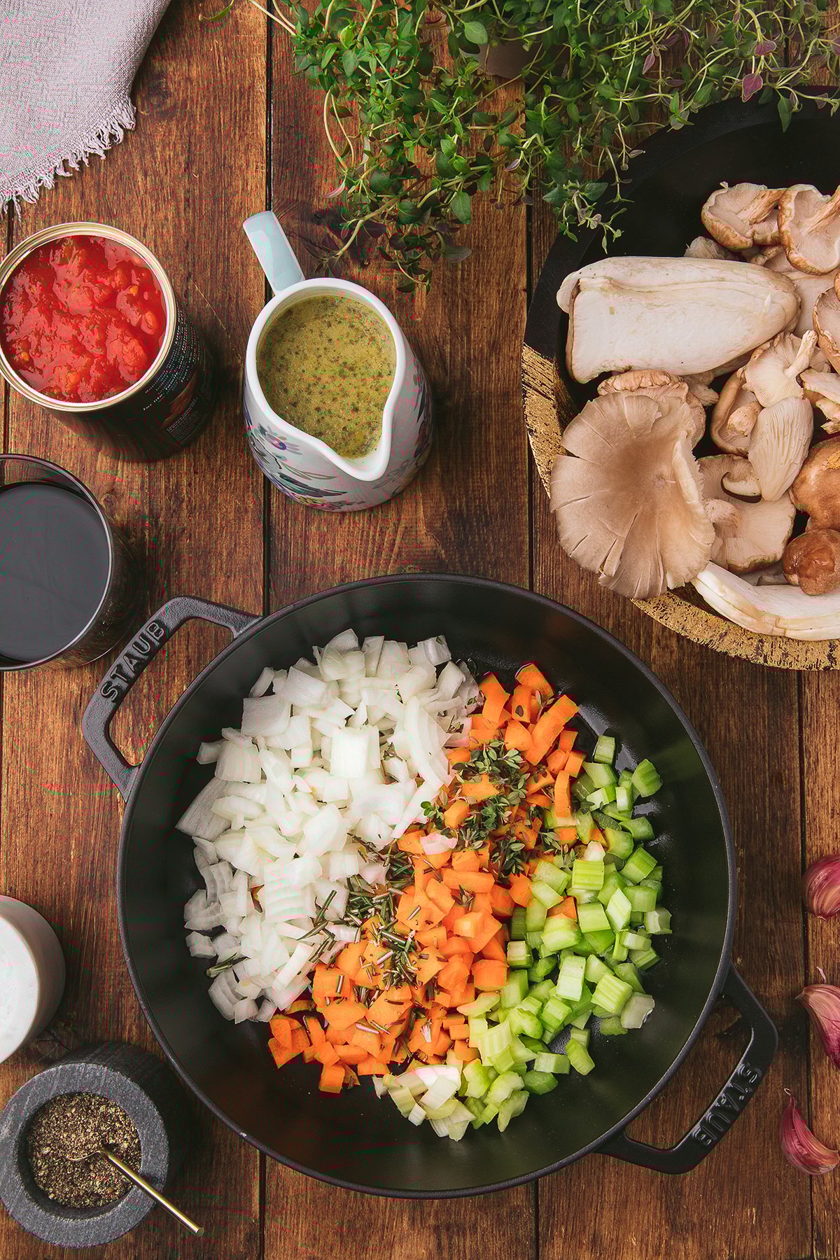 Chopped onions, carrots, and celery in a pot, surrounded by mushrooms, herbs, canned tomatoes, and broth—perfect for crafting the best ragu recipe or a hearty Vegan Pasta Sauce like classic Mushroom Ragu.