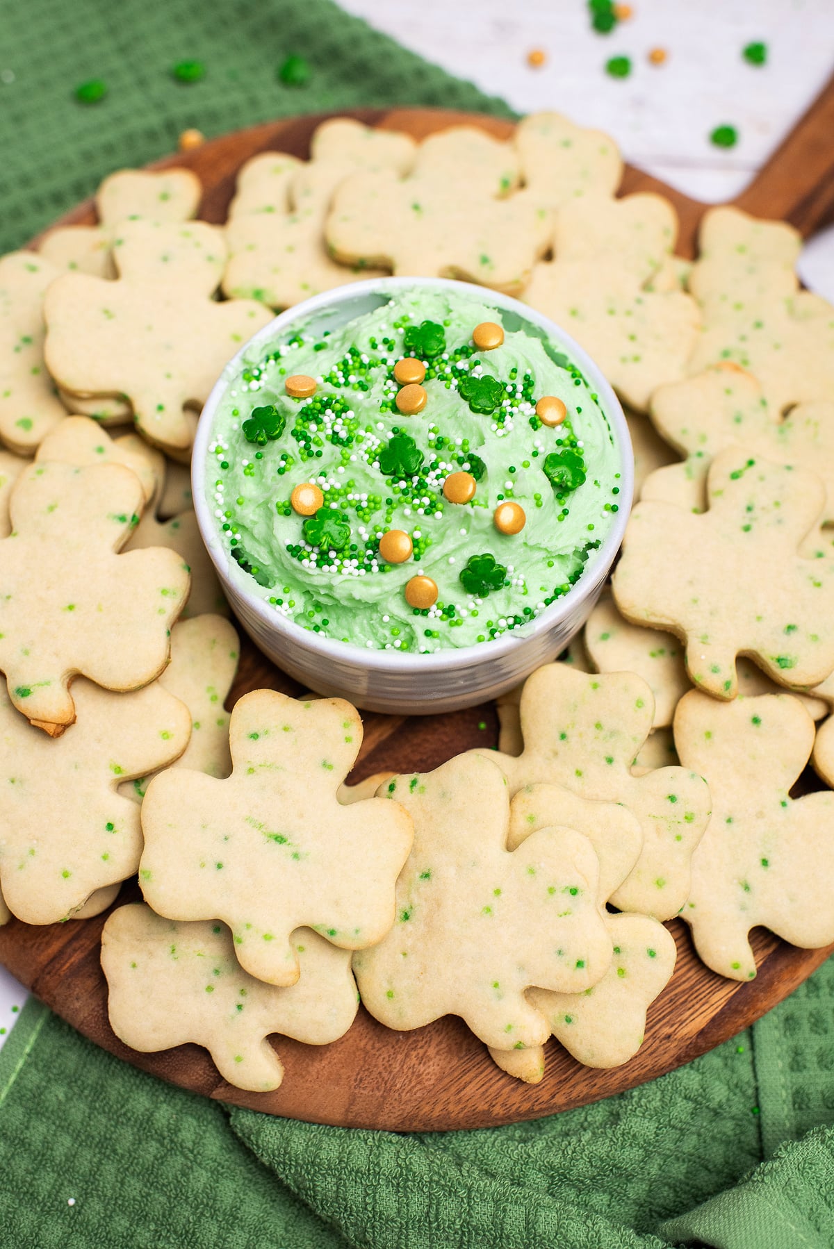 Shamrock-shaped cookies surround a bowl of green frosting topped with gold and white sprinkles—a festive St. Patrick's Cookies and Buttercream Dip inspired by the classic Dunkaroos, perfect for your St. Patrick's Day cookie recipe collection.