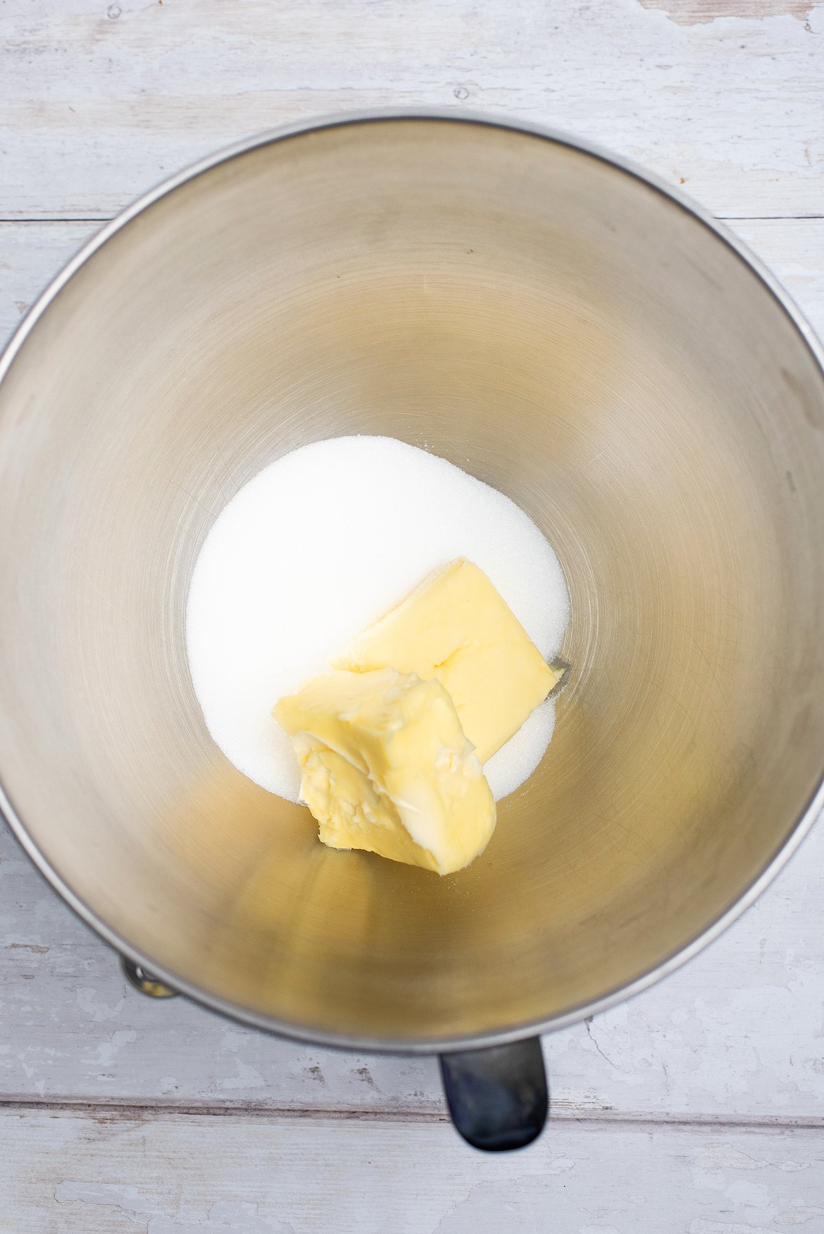 Butter and granulated sugar in a metal mixing bowl on a light-colored wooden surface, ready to create festive shamrock sugar cookies or pair with a creamy St. Patrick's Cookies and Buttercream Dip for a Dunkaroos-inspired treat.