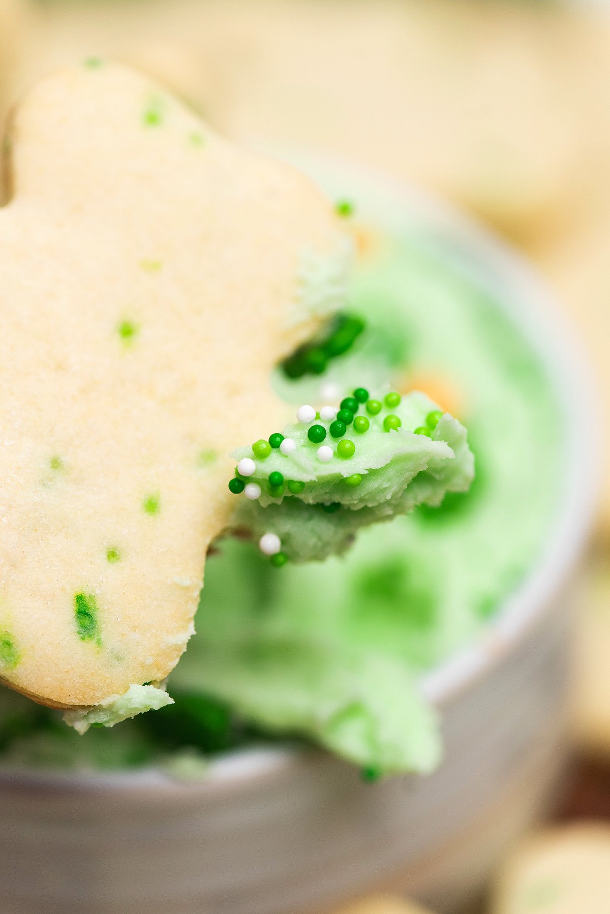 A shamrock-shaped sugar cookie with green flecks, partially dipped in green ice cream with festive sprinkles—perfect for St. Patty's party ideas or as a sweet treat alongside St. Patrick's Cookies and Buttercream Dip.