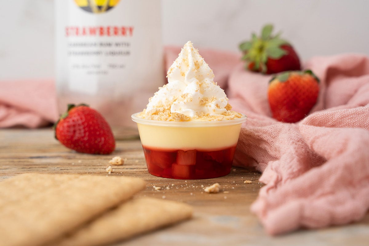 A cup of strawberry ice cream with [strawberry dessert cocktail] crackers next to a bottle of bourbon.