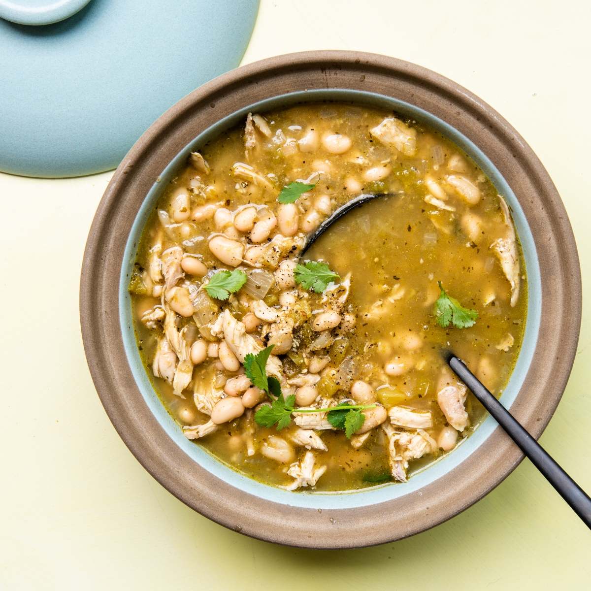 A bowl of Mexican inspired white bean chicken chili garnished with cilantro, with a spoon resting inside—perfect for fans of green chili soup.