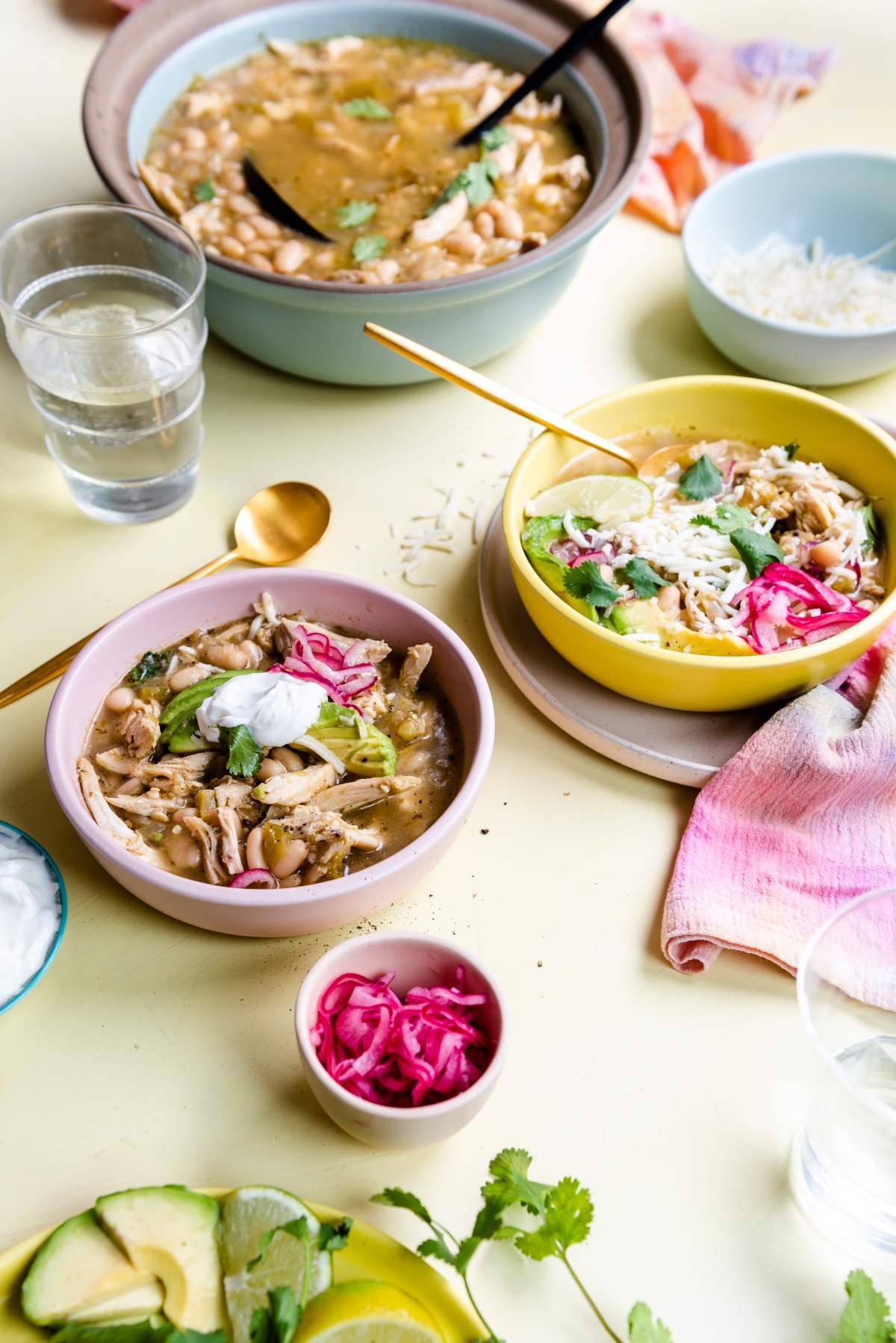 Bowls of Mexican-inspired chili verde chicken soup topped with sour cream, cilantro, and pickled onions, served with rice and avocado.