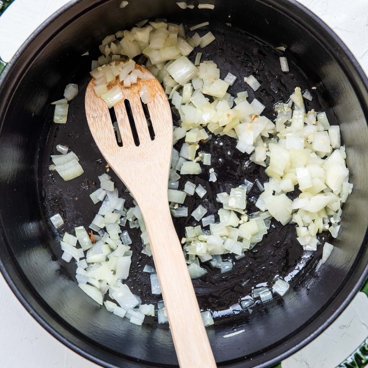Chopped onions being sautéed in a black pan with a wooden spoon—the perfect start to a flavorful White Bean Green Chile Chicken Soup.