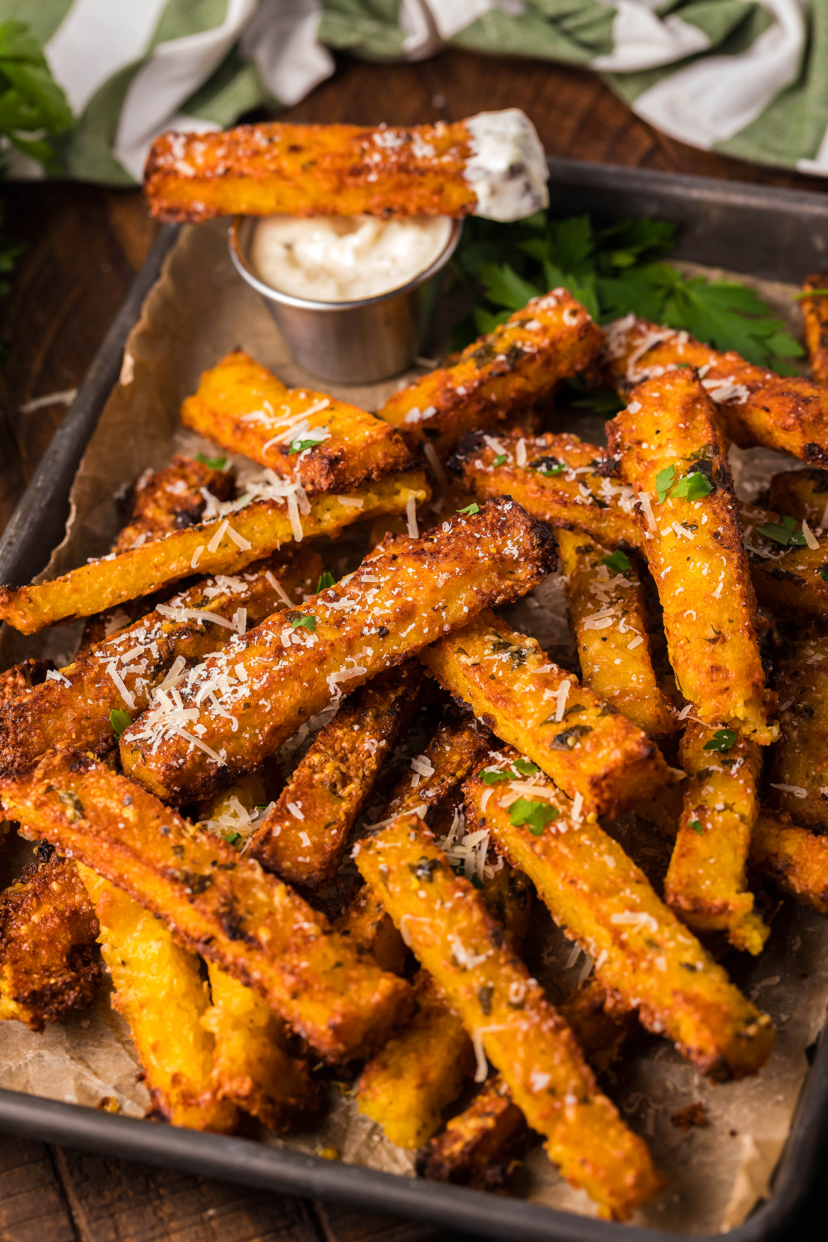 A tray of crispy air fried polenta fries, topped with grated cheese and herbs, served with a cup of rich truffle mayo dipping sauce.