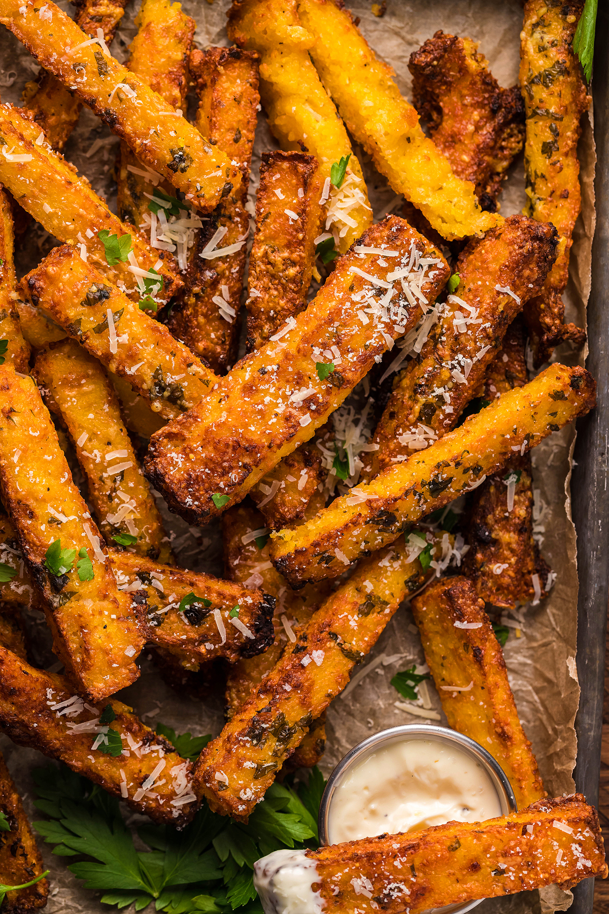 Crispy air fried polenta fries topped with grated cheese and herbs, served with a side of creamy dipping sauce—perfect as a tasty side dish or appetizer.