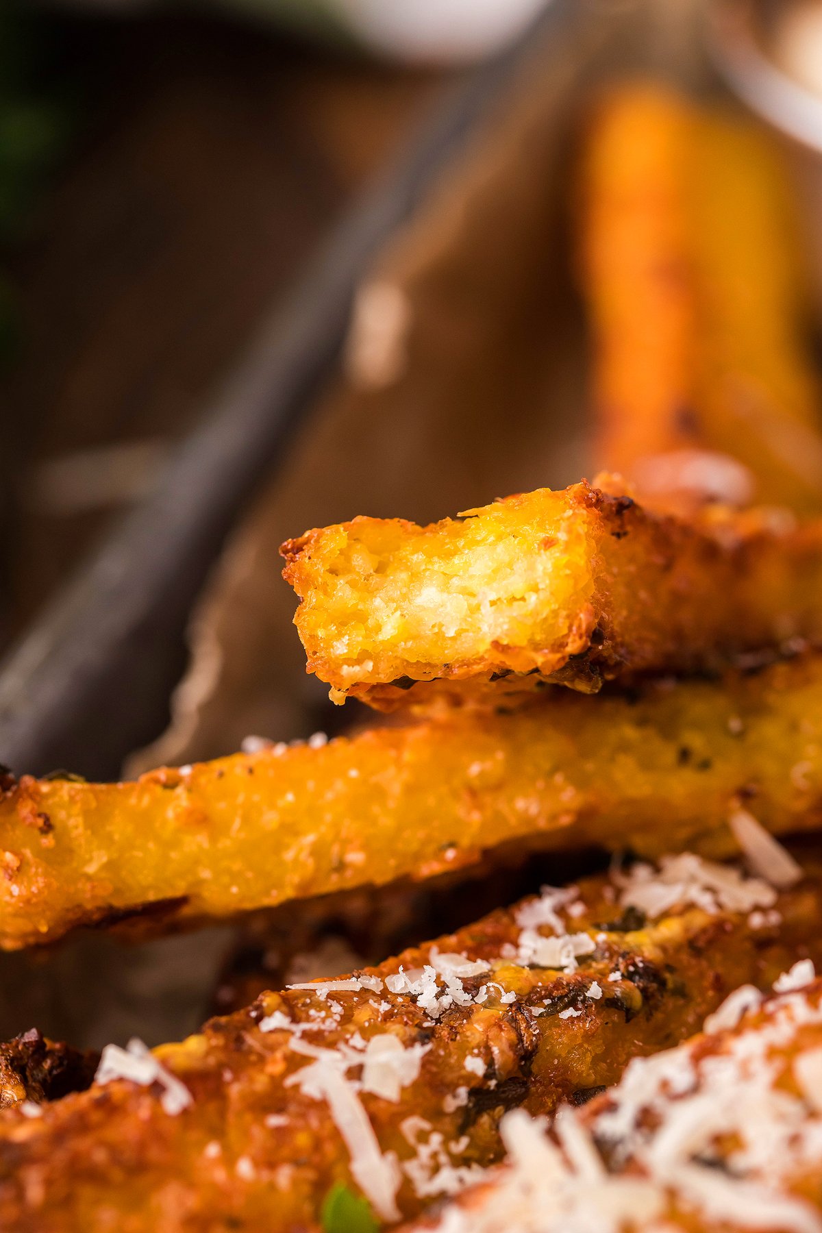 Close-up of crispy golden Air Fryer Polenta Fries topped with grated cheese on a brown parchment-lined tray, served as a flavorful side dish or appetizer.