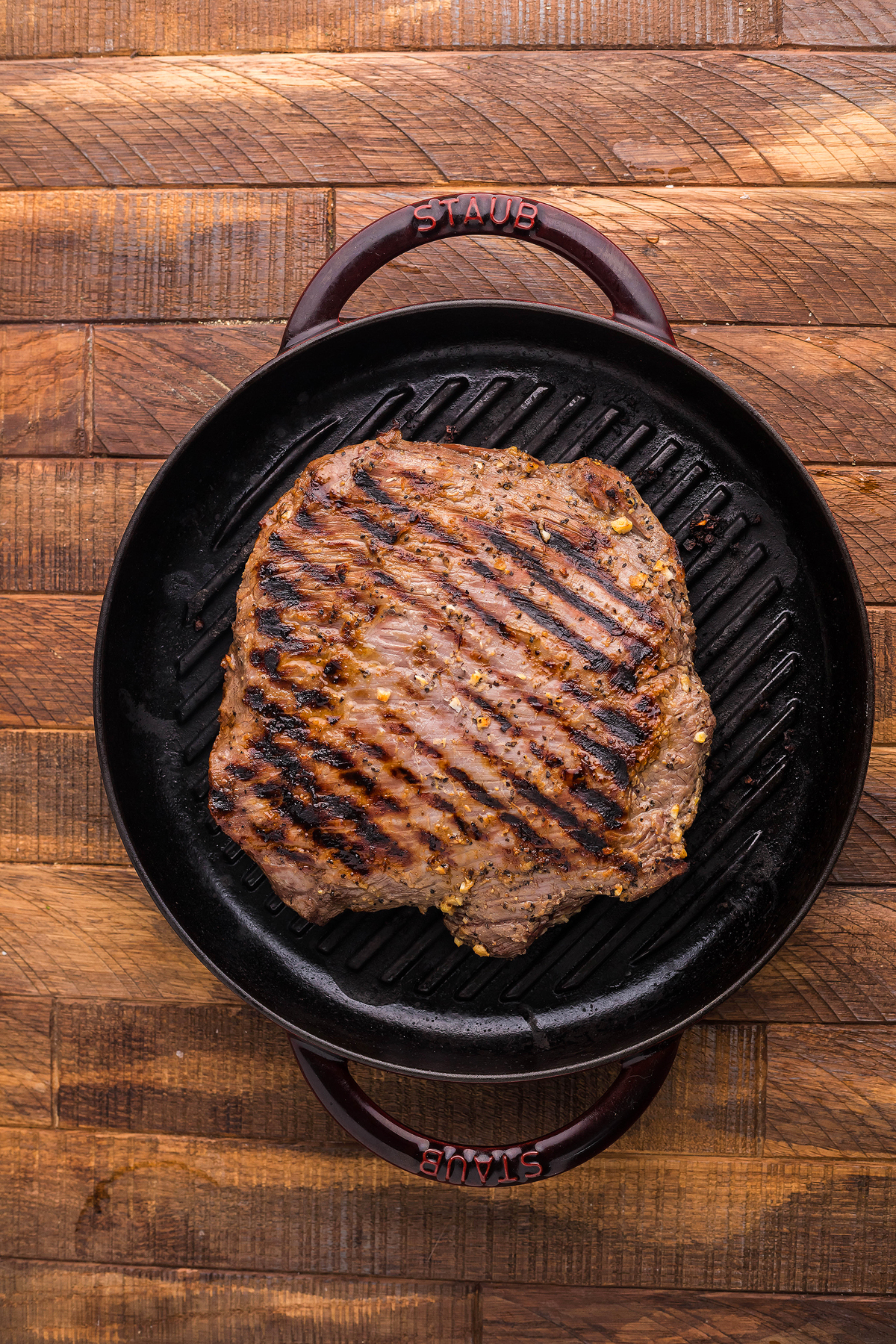 Grilled flank steak on a cast iron grill pan, beautifully seared and set on a wooden surface—perfect for a quick steak dinner.