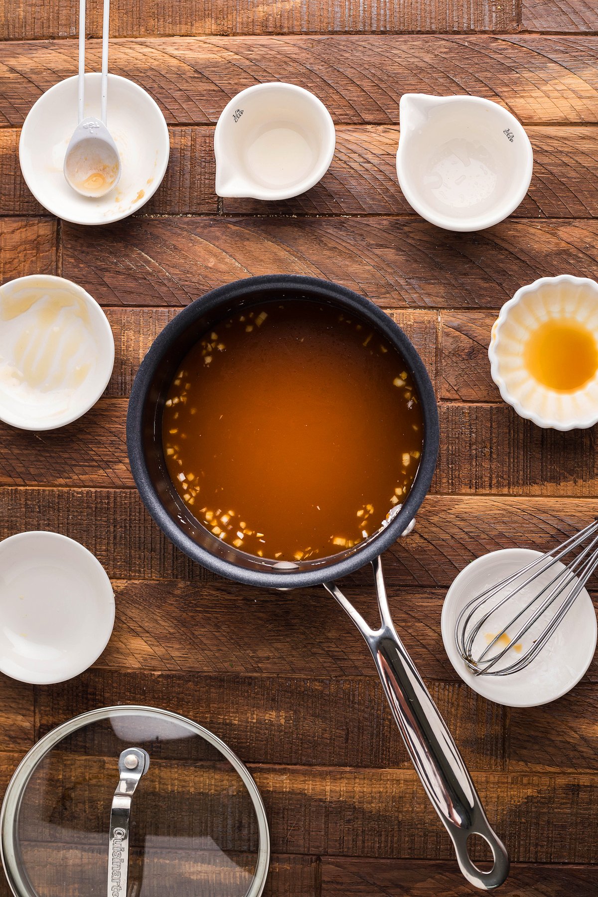 A saucepan with brown sauce sits on a wooden surface, surrounded by empty bowls, utensils, and a delicious Teriyaki Flank Steak and Veggies flank steak recipe ready to be served.
