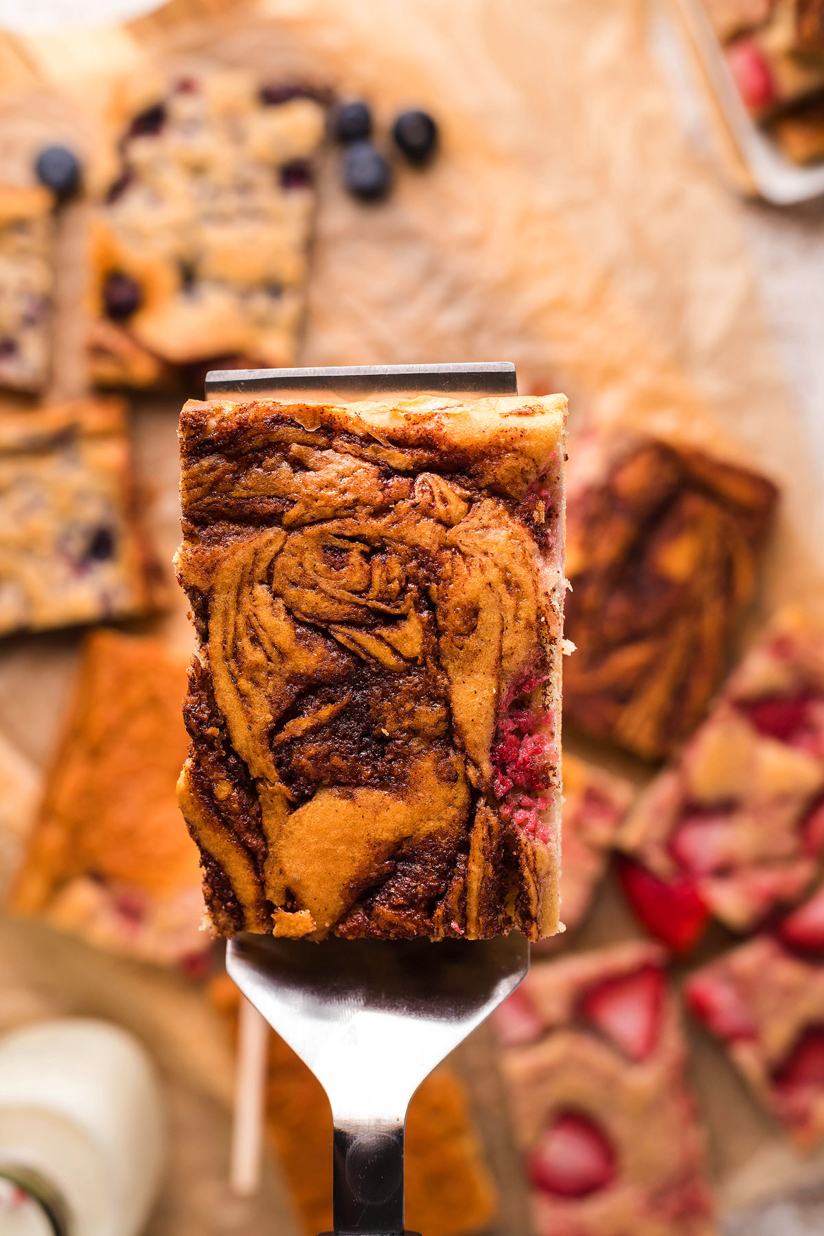 A close-up of a marbled dessert bar on a spatula, inspired by the pancakes baked in the oven trend, with more dessert bars blurred in the background.