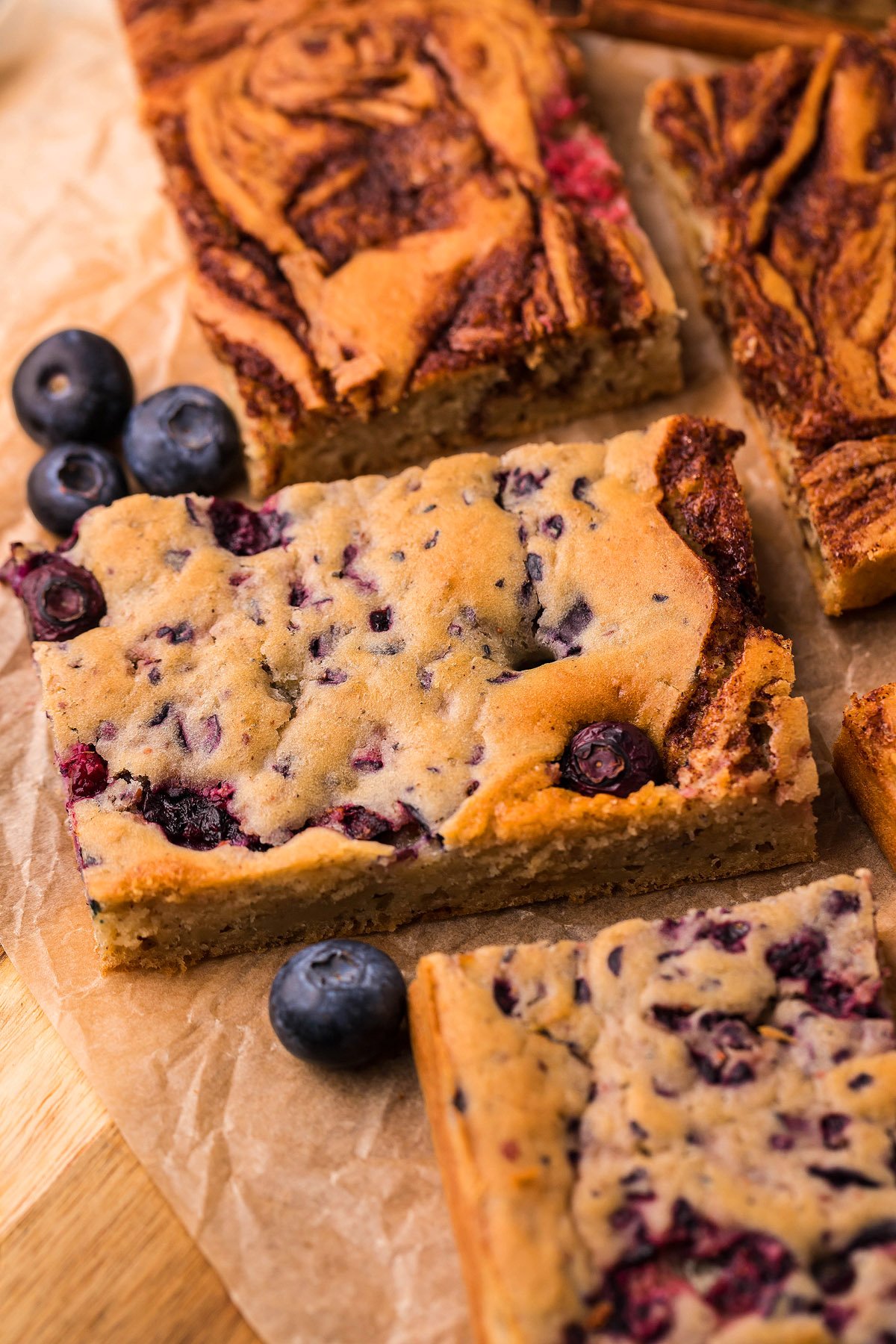 A close-up of blueberry cake bars on parchment paper, garnished with fresh blueberries—these treats are inspired by the Tik Tok recipe trend for Sheet Pan Buttermilk Pancakes.