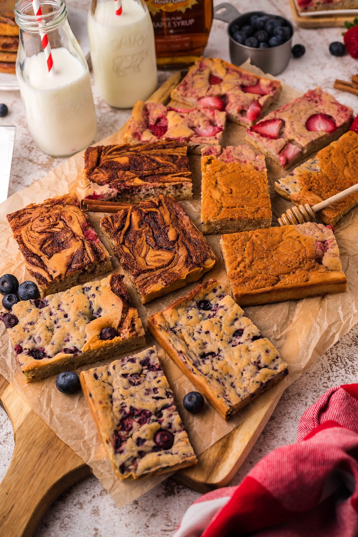 A variety of berry and chocolate breakfast bars are arranged on parchment, alongside bottles of milk and fresh berries—perfect for pairing with pancakes baked in the oven like delicious Sheet Pan Buttermilk Pancakes.