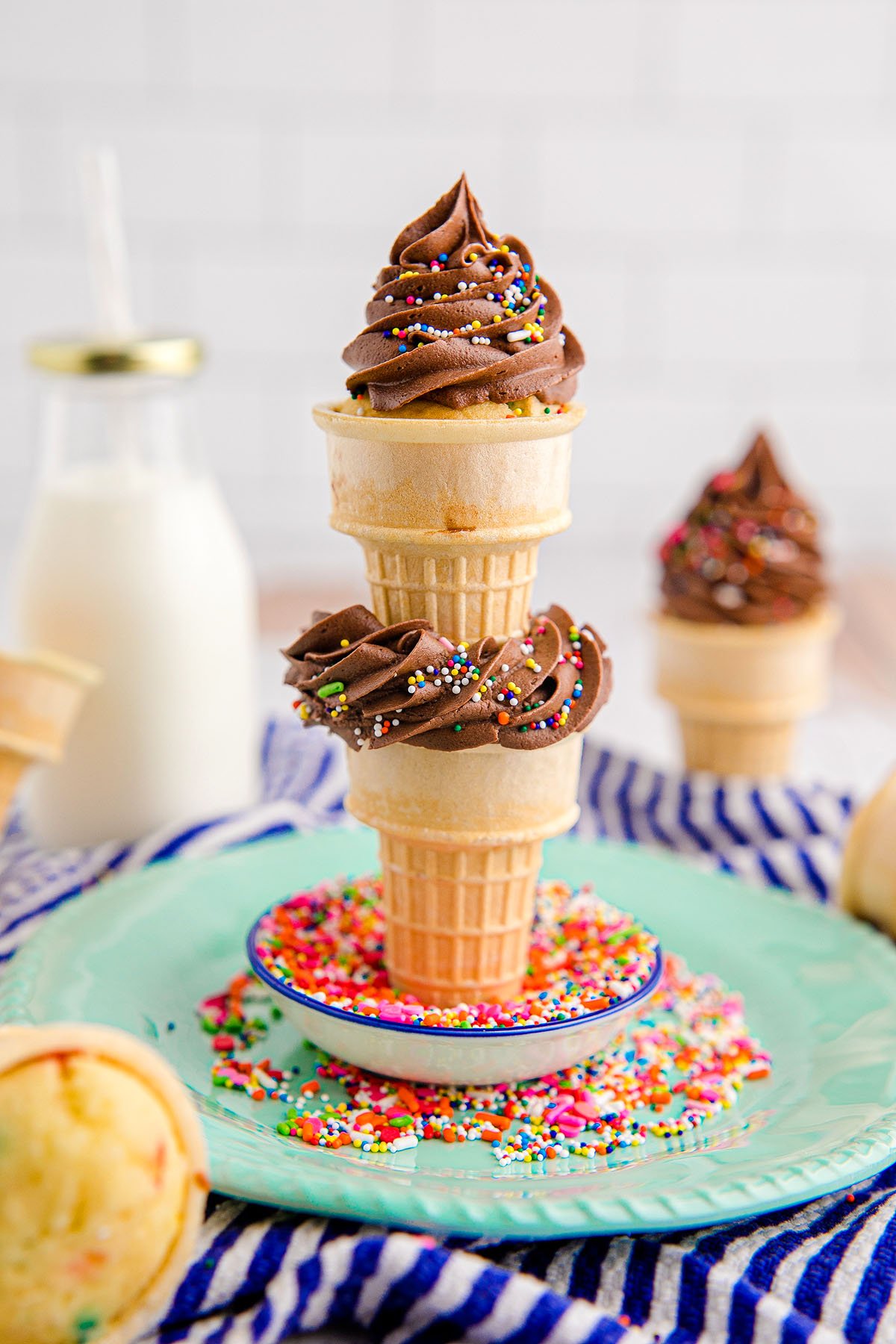 Three Ice Cream Cone Cupcakes with chocolate frosting and colorful sprinkles are stacked on a plate—perfect cupcakes for birthday parties and sure to delight guests of all ages.