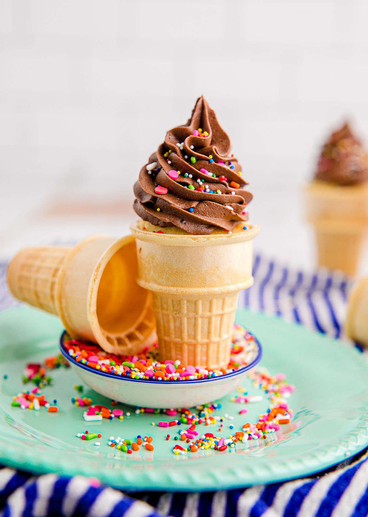 Chocolate soft serve in a cone, inspired by cupcakes in ice cream cones, topped with colorful sprinkles and served on a plate with extra funfetti cake mix sprinkles.