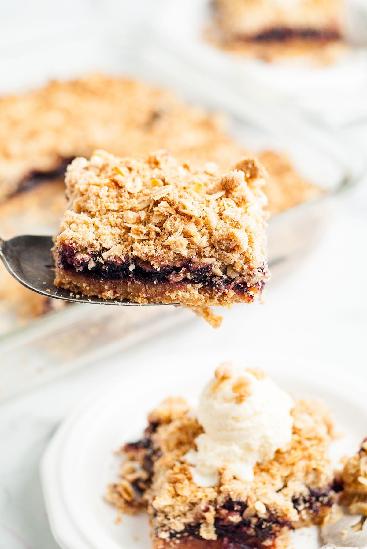 A spatula lifts a crumbly cherry pie bar above a plate with another bar topped with a scoop of vanilla ice cream—a delicious Starbucks copycat recipe.