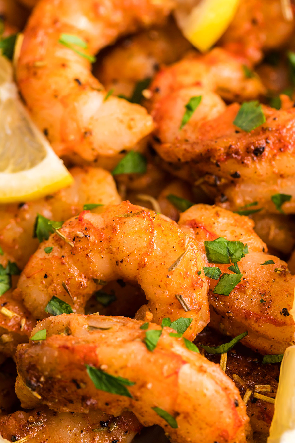Close-up of smoked shrimp, seasoned with homemade blackening seasoning, garnished with chopped parsley and lemon wedges.