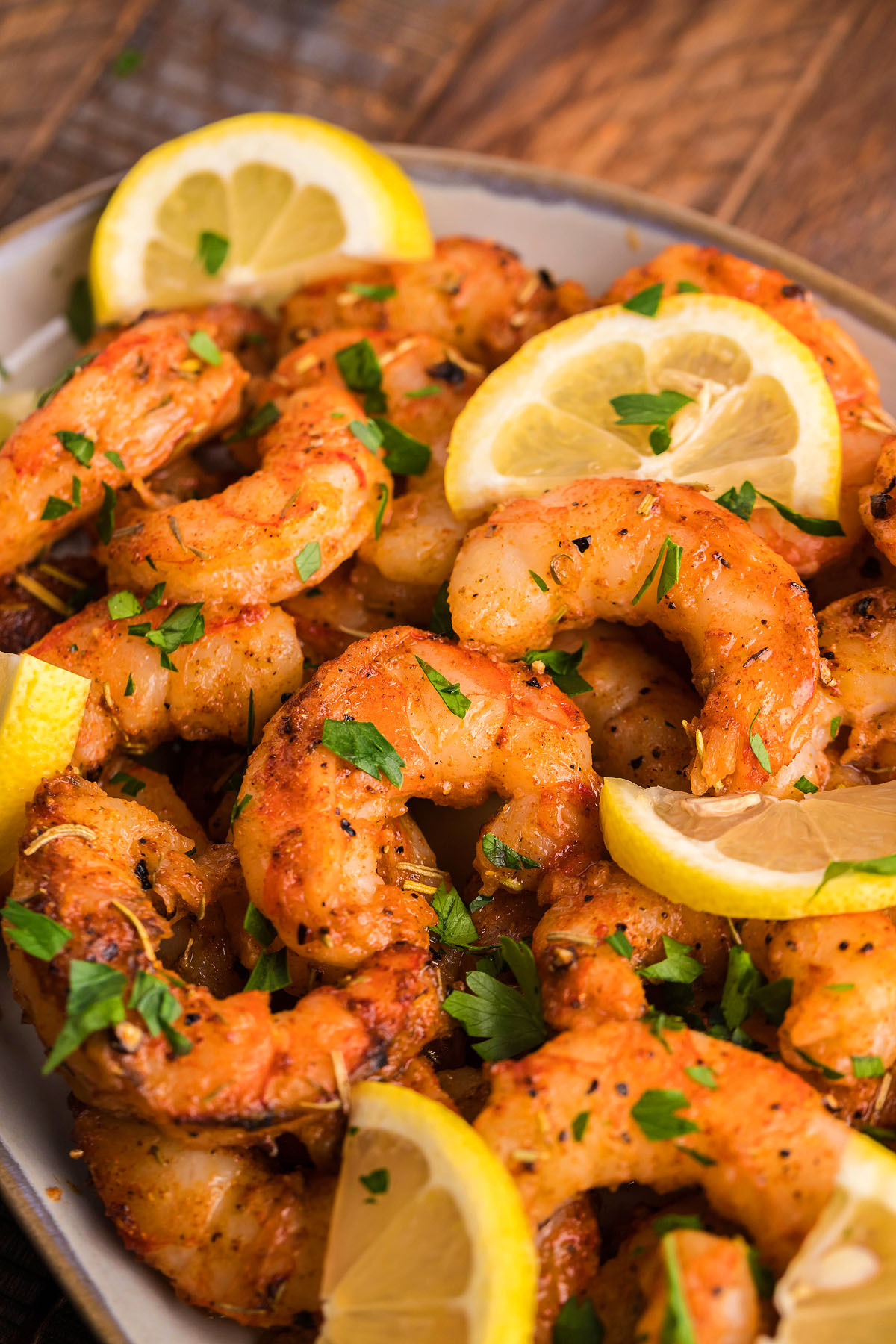 Grilled shrimp coated in homemade blackening seasoning, garnished with chopped parsley and lemon slices on a plate.