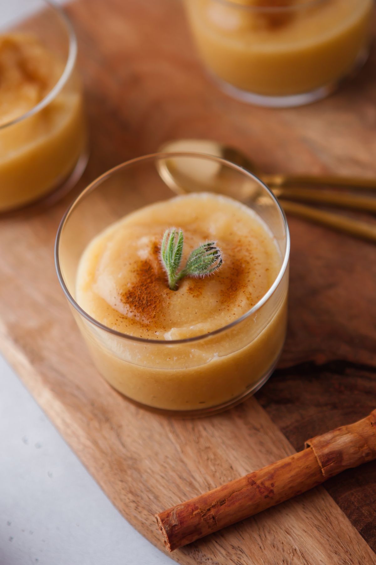 A glass of creamy guava flavoured applesauce dessert topped with cinnamon and a sprig sits on a wooden board, with a cinnamon stick nearby.