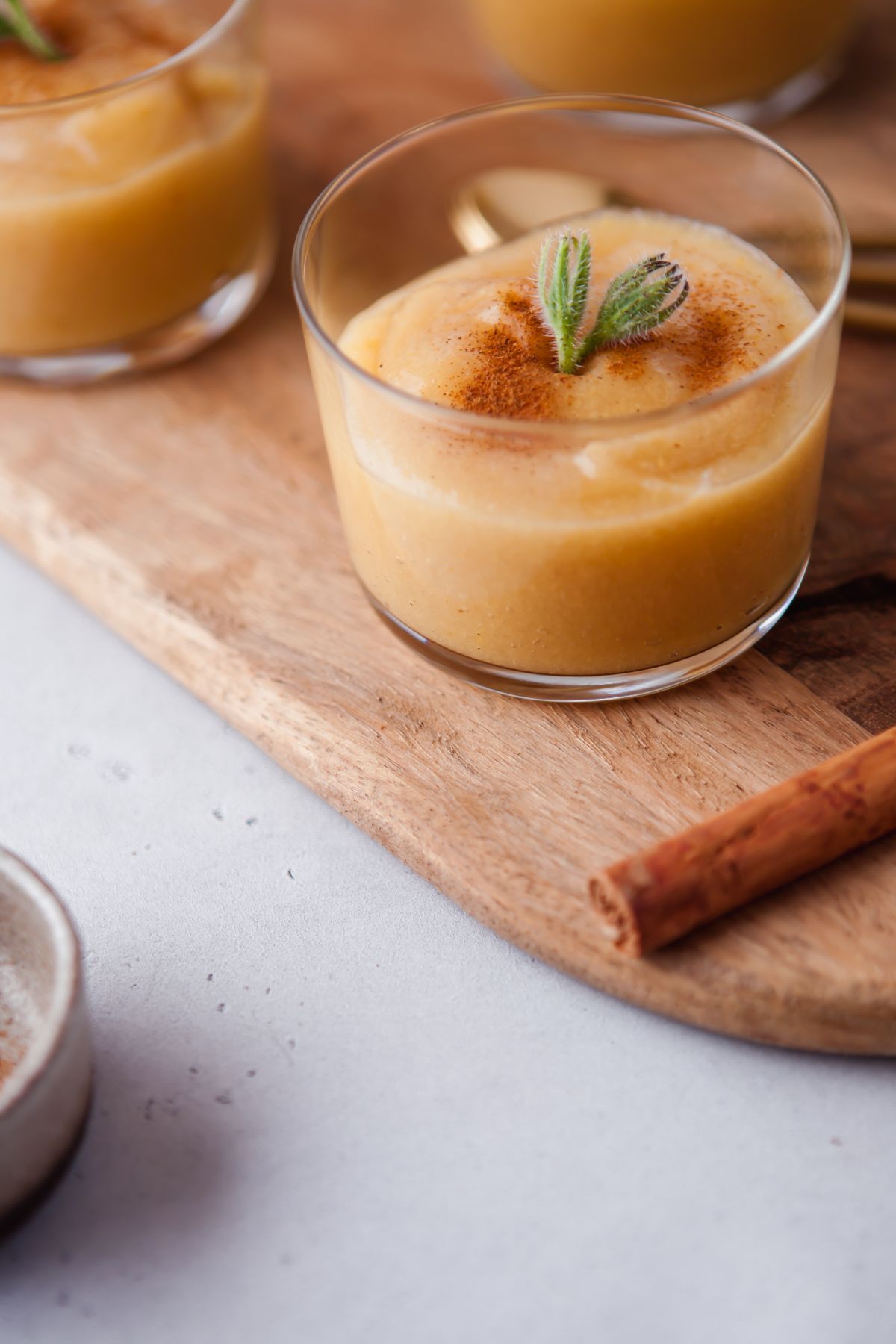 A glass of creamy dessert topped with cinnamon and a mint sprig on a wooden board, featuring a hint of Guava Applesauce for a unique twist.