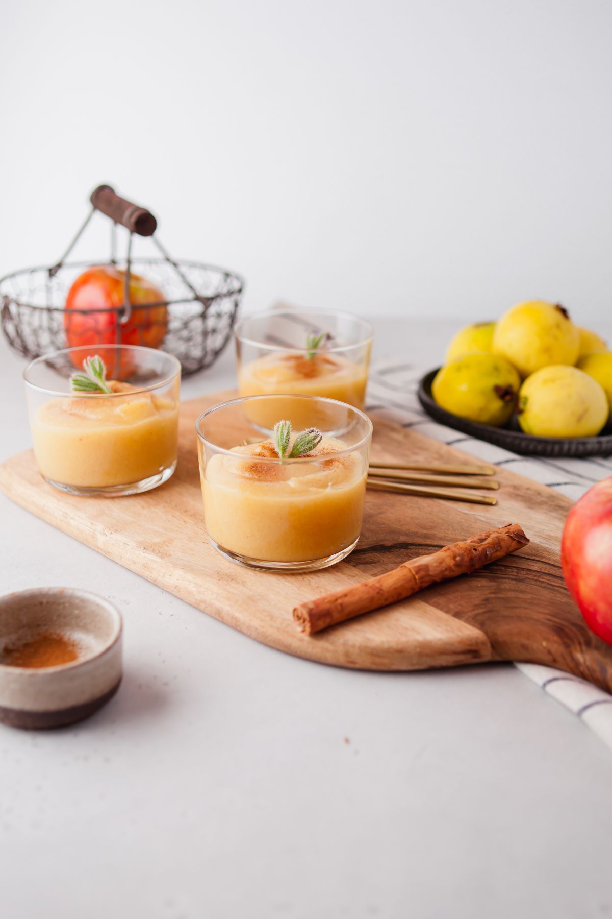 Three glasses of applesauce from scratch with mint leaves on a wooden board, surrounded by apples, quinces, and cinnamon sticks—perfect for trying unique applesauce variations.