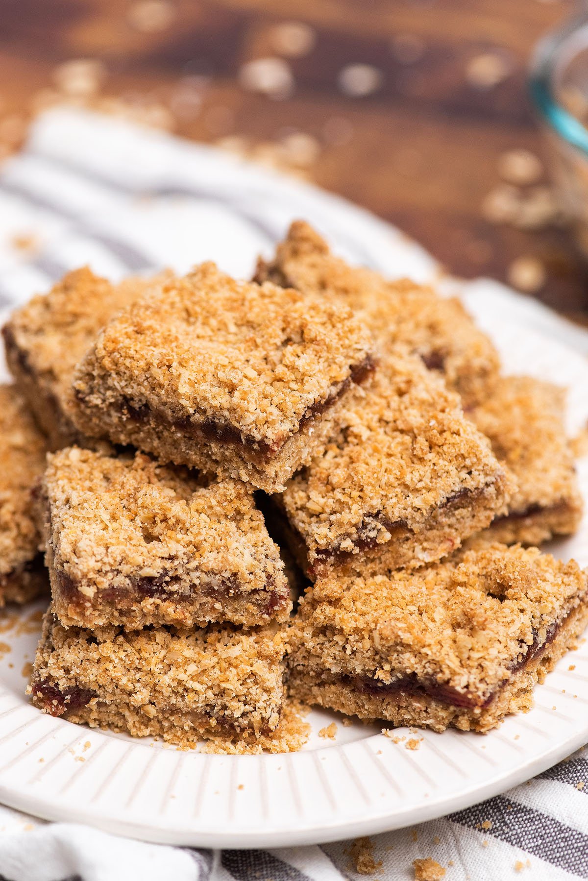 A plate stacked with several oat crumble bars filled with a dark fruit layer—these classic Date Bars feature a delicious Oatmeal Crumble Topping, making them the perfect recipe with dates for any treat lover.