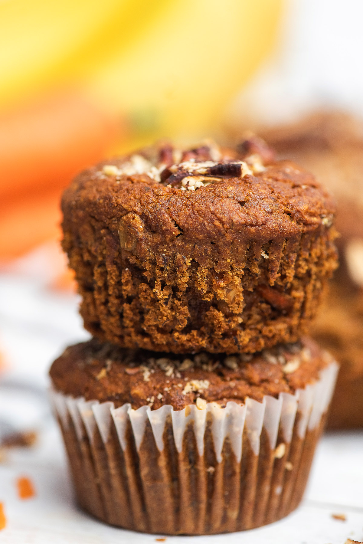 Two gluten free muffins stacked on top of each other, with chopped nuts on top, in paper liners—perfect for a Morning Glory Muffins-inspired treat.