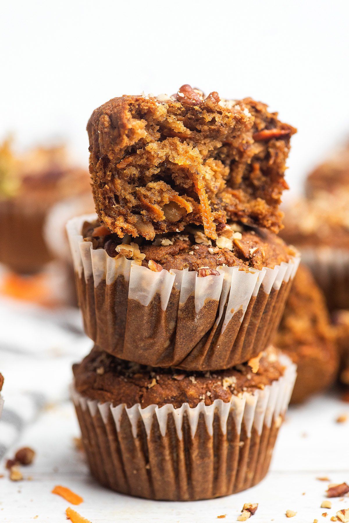 A stack of two Morning Glory Muffins, with the top gluten free muffin bitten into, reveals a moist, textured interior.