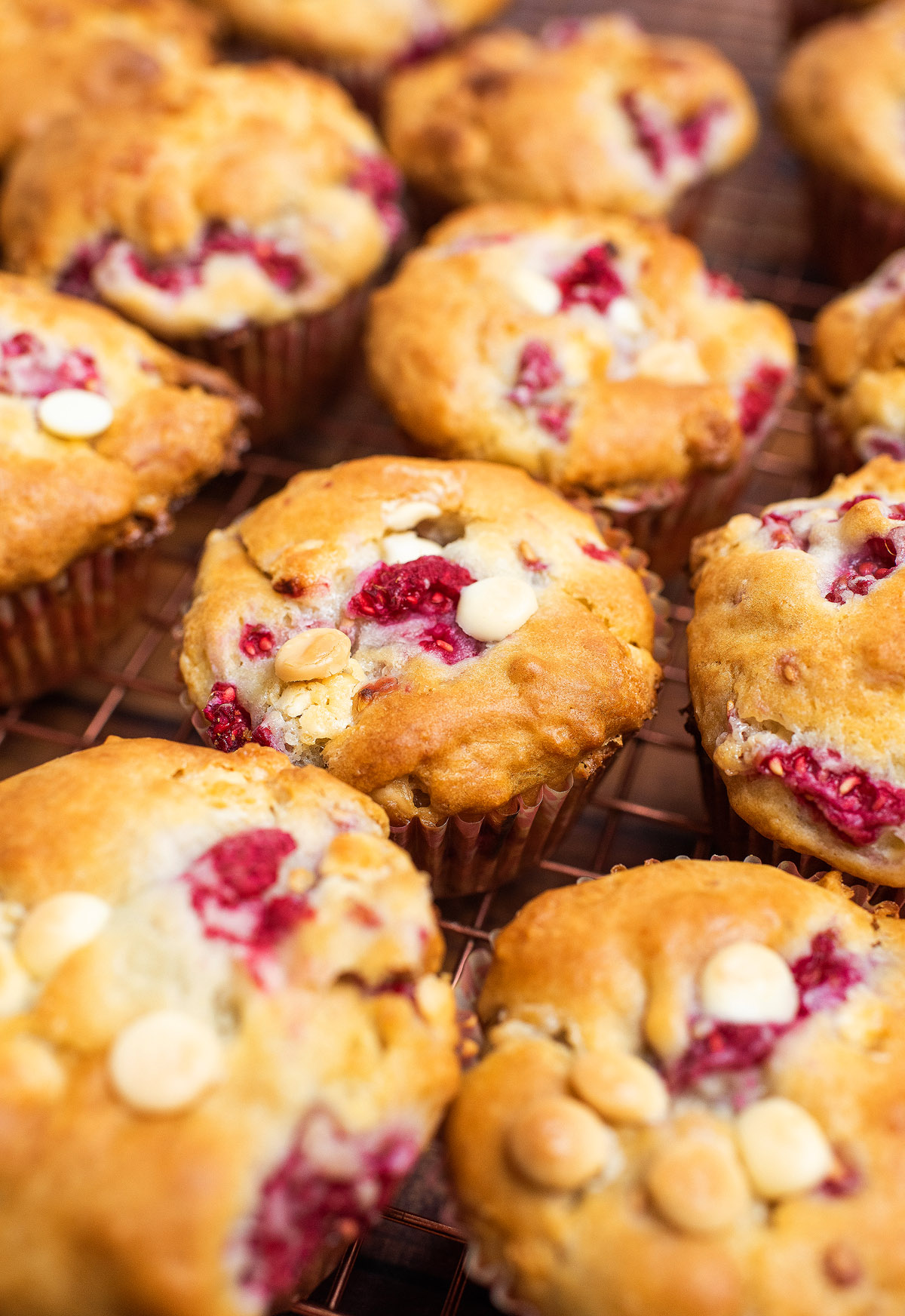 Golden raspberry white chocolate muffins dotted with creamy chips rest on a cooling rack, perfectly baked and irresistible.