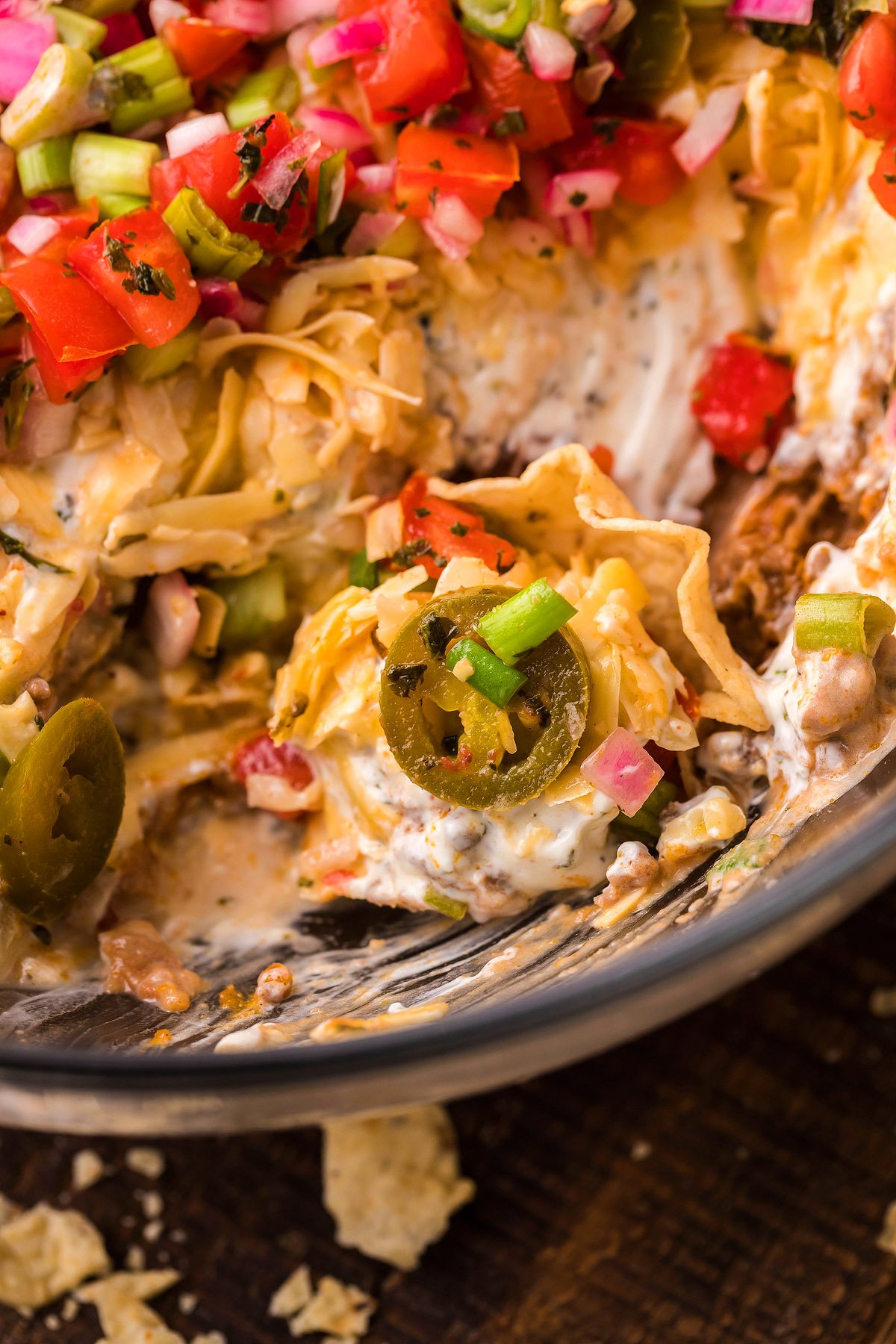 Close-up of a creamy Mexican layered dip with shredded cheese, jalapeños, chopped tomatoes, green onions, and savory ground beef—perfect for your next 5 Layer Taco Dip.