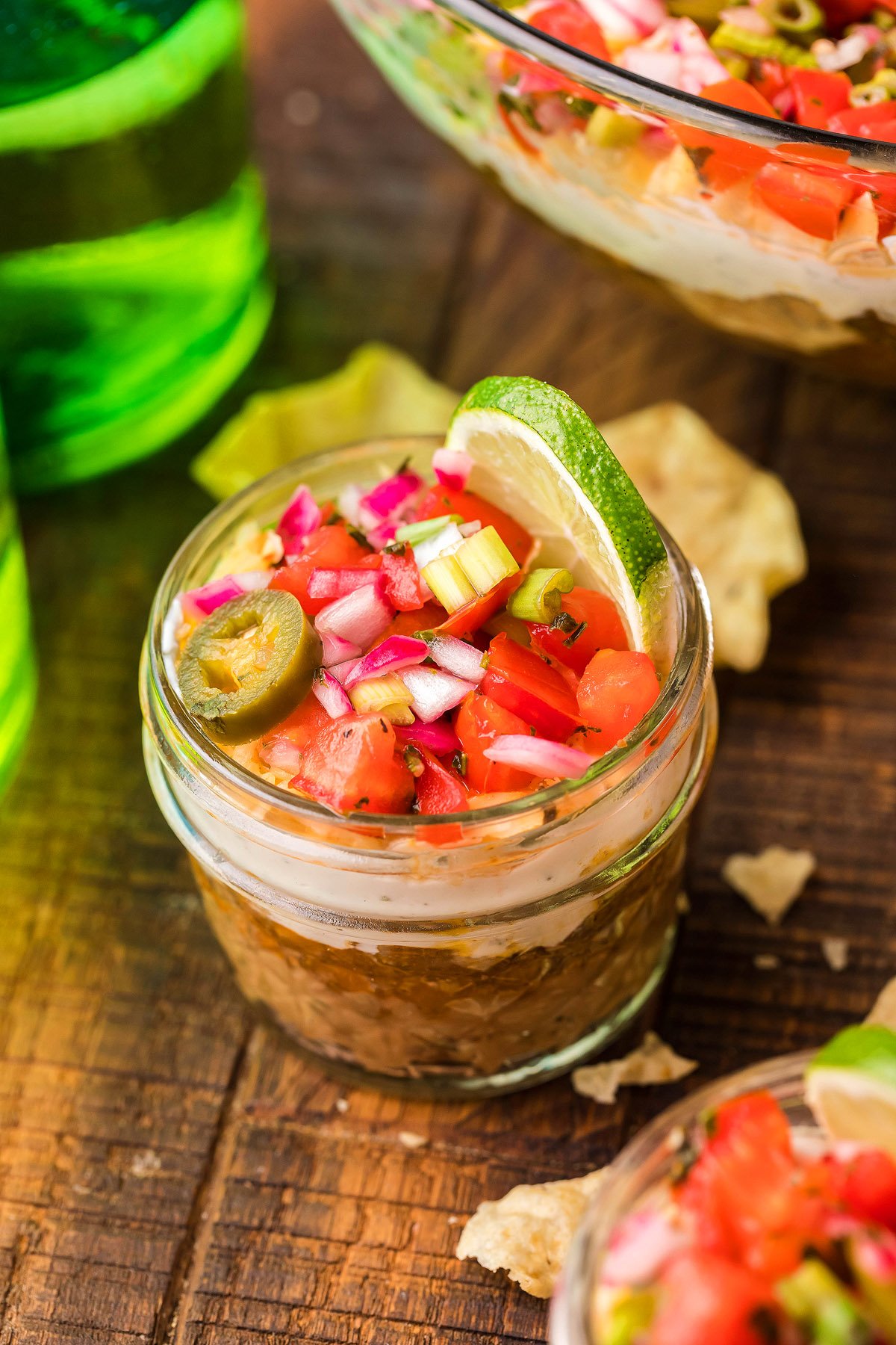 Jar filled with beefy taco dip, topped with diced veggies, jalapeño, and a lime wedge—an easy appetizer perfect for any occasion, served on a wooden table.