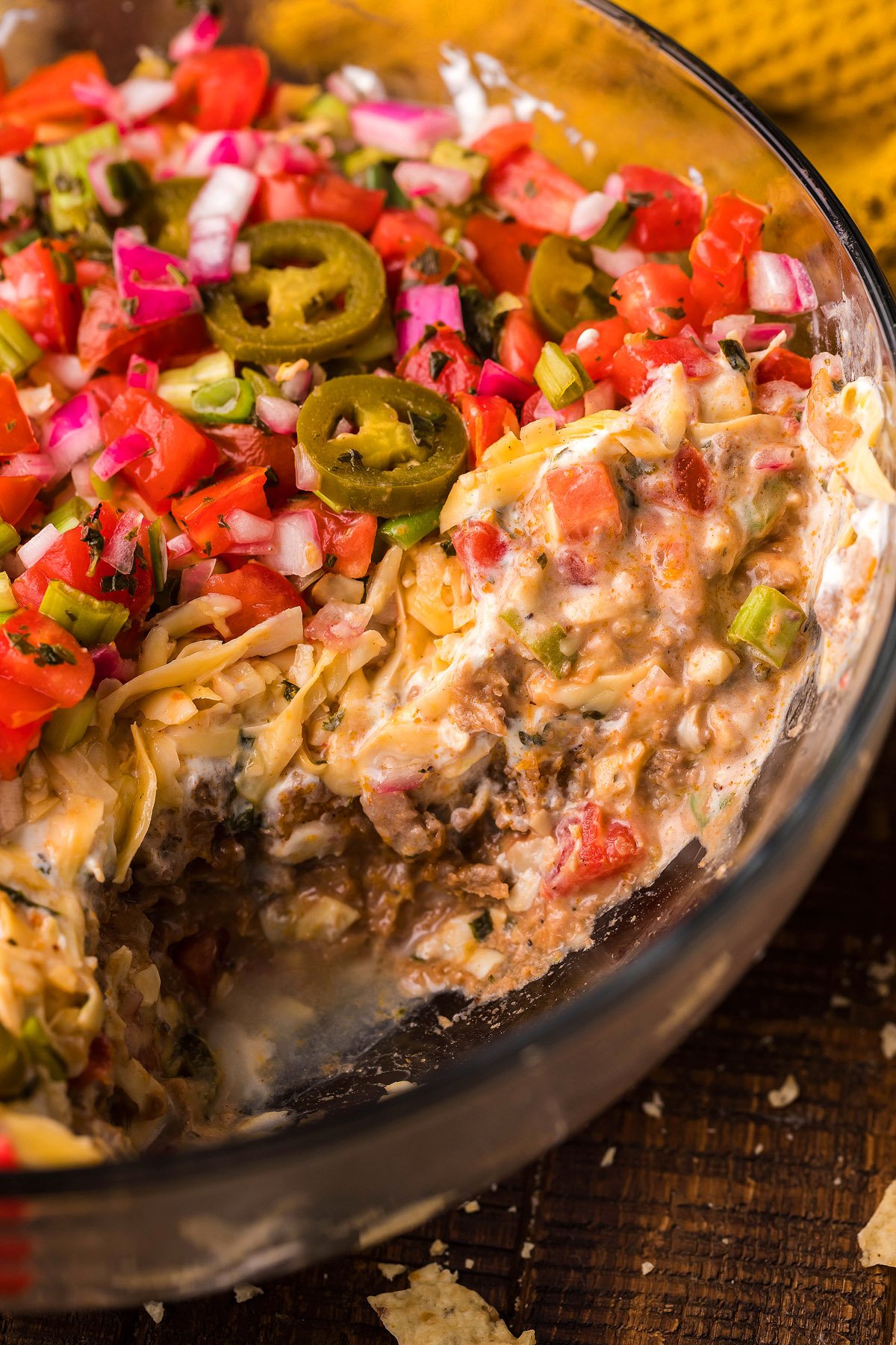 A glass bowl of beefy taco dip, layered and topped with diced tomatoes, red onions, jalapeños, and shredded cheese—an easy appetizer perfect for any gathering.