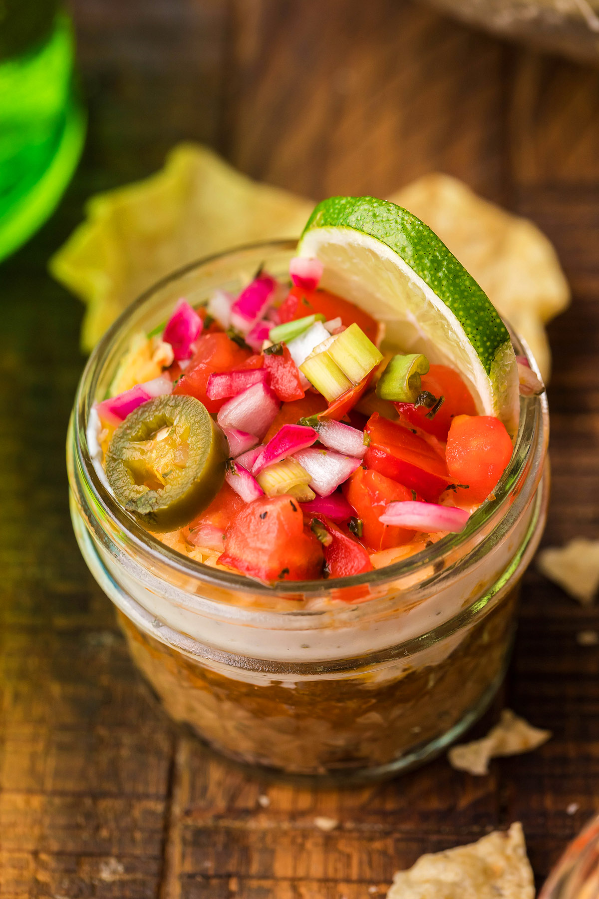A jar of salsa topped with diced vegetables, a jalapeño slice, and a lime wedge on a wooden table—perfect for serving as part of an easy appetizer or your favorite Mexican layered dip.