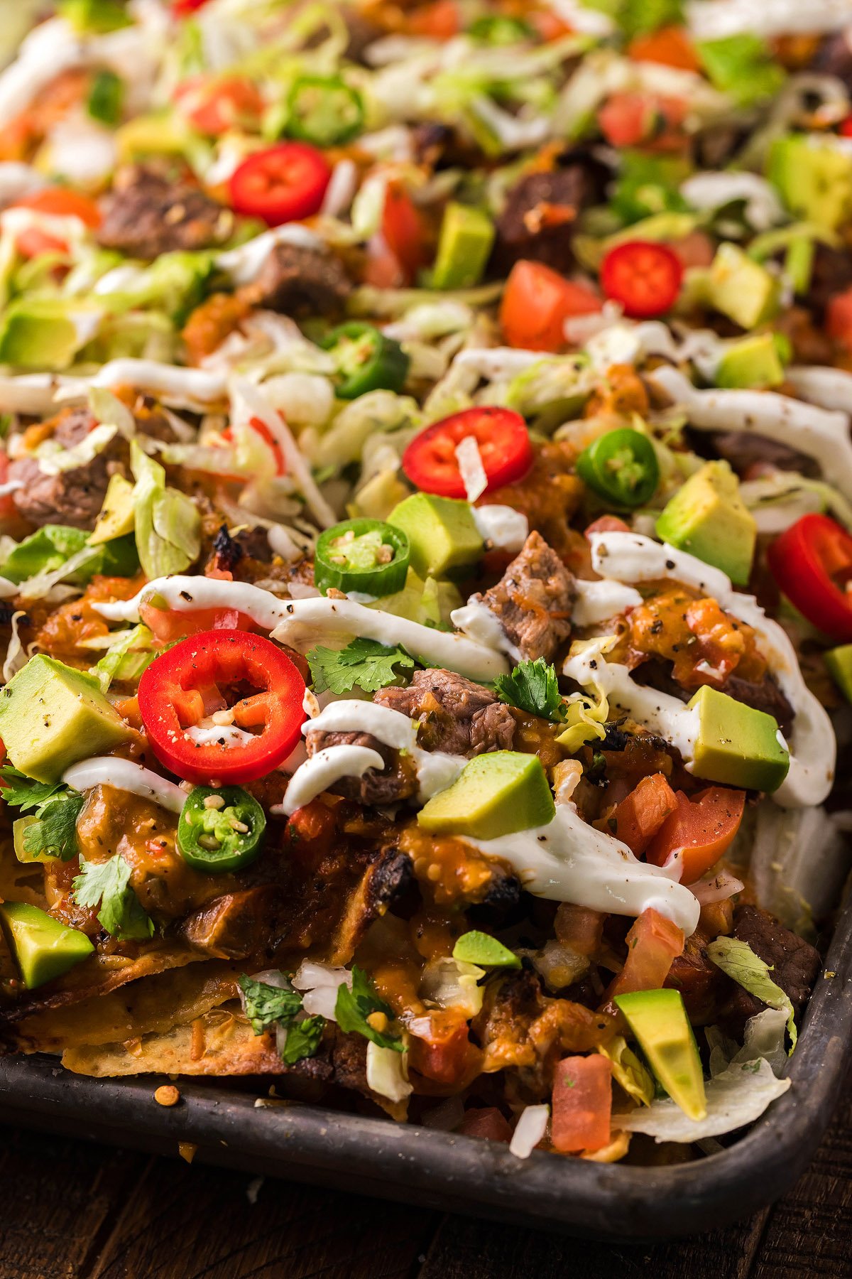 Loaded Seared Steak Nachos topped with diced avocado, jalapeños, tomatoes, cilantro, homemade salsa, and drizzled with sour cream—an irresistible mix of nacho toppings in every bite.
