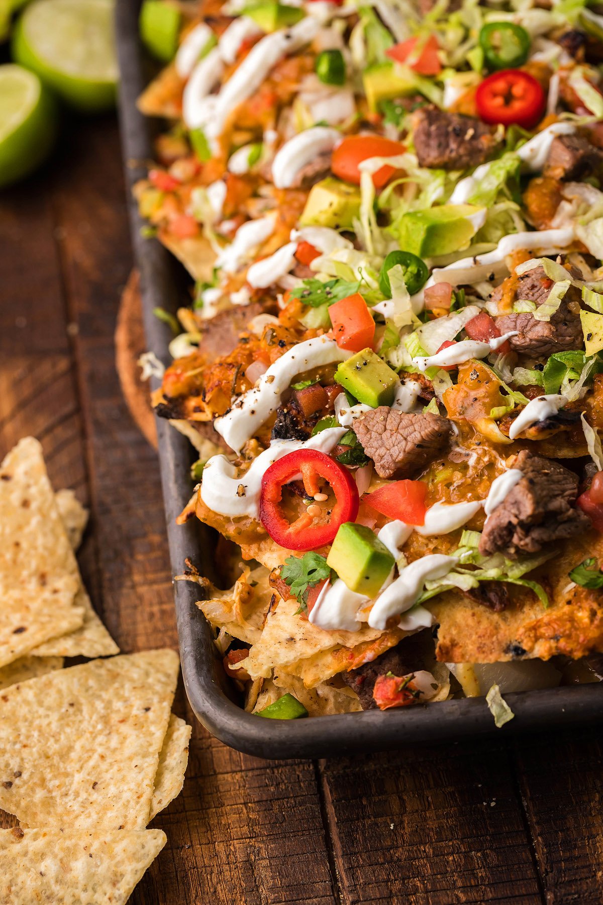 Sheet pan Mexican steak nachos loaded with cheese, sour cream, lettuce, tomatoes, jalapeños, red chili slices, and all your favorite nacho toppings. Perfect when paired with fresh Tomatillo Serrano Salsa!.