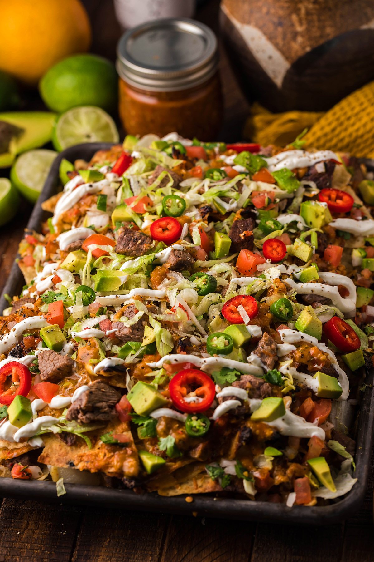 Sheet pan nachos topped with beef, avocado, tomatoes, jalapeños, shredded lettuce, and drizzled with sour cream—perfect when paired with homemade salsa for an extra burst of flavor.