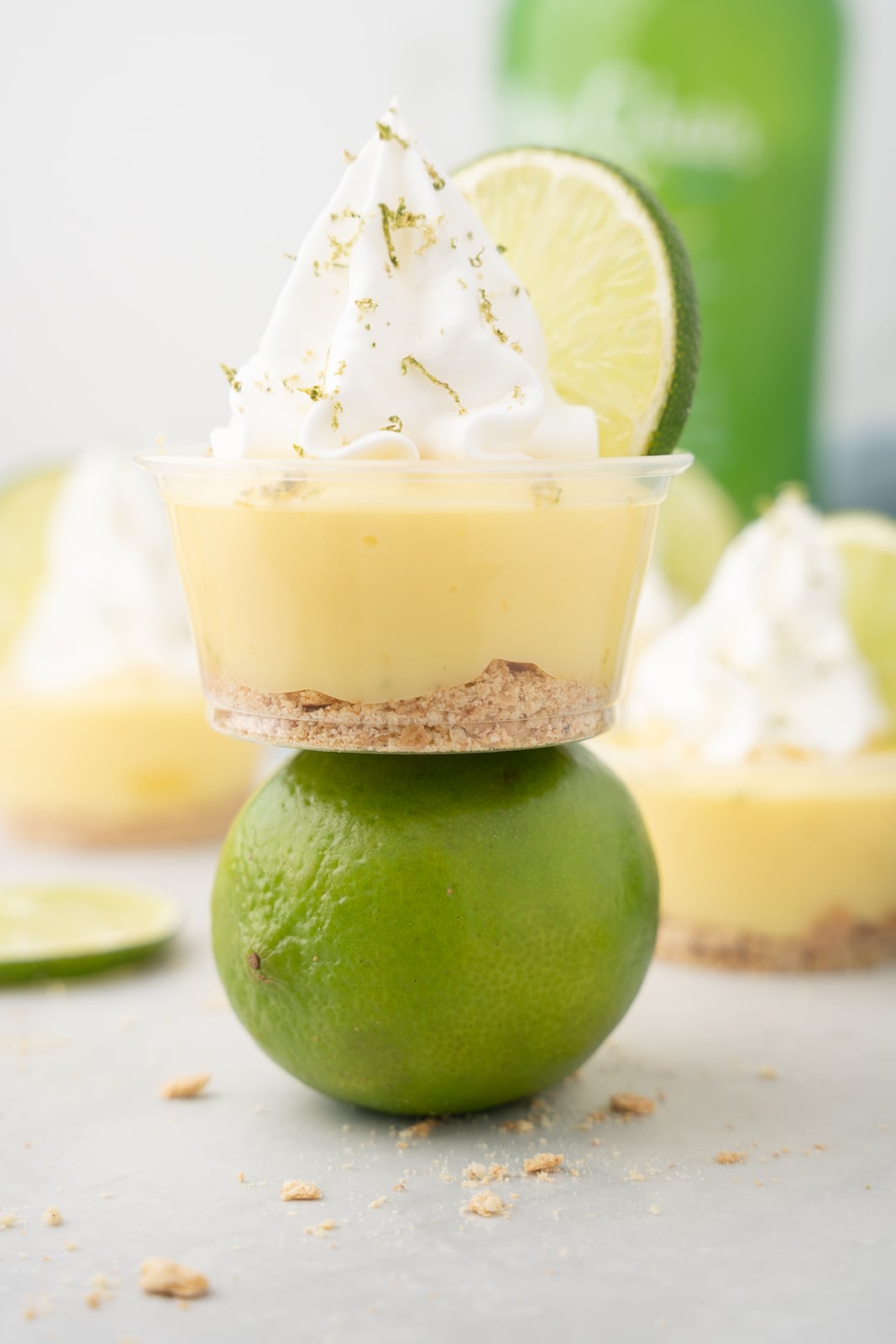 Key lime pudding shot in a cup with whipped cream and lime slice, balanced on a whole lime.
