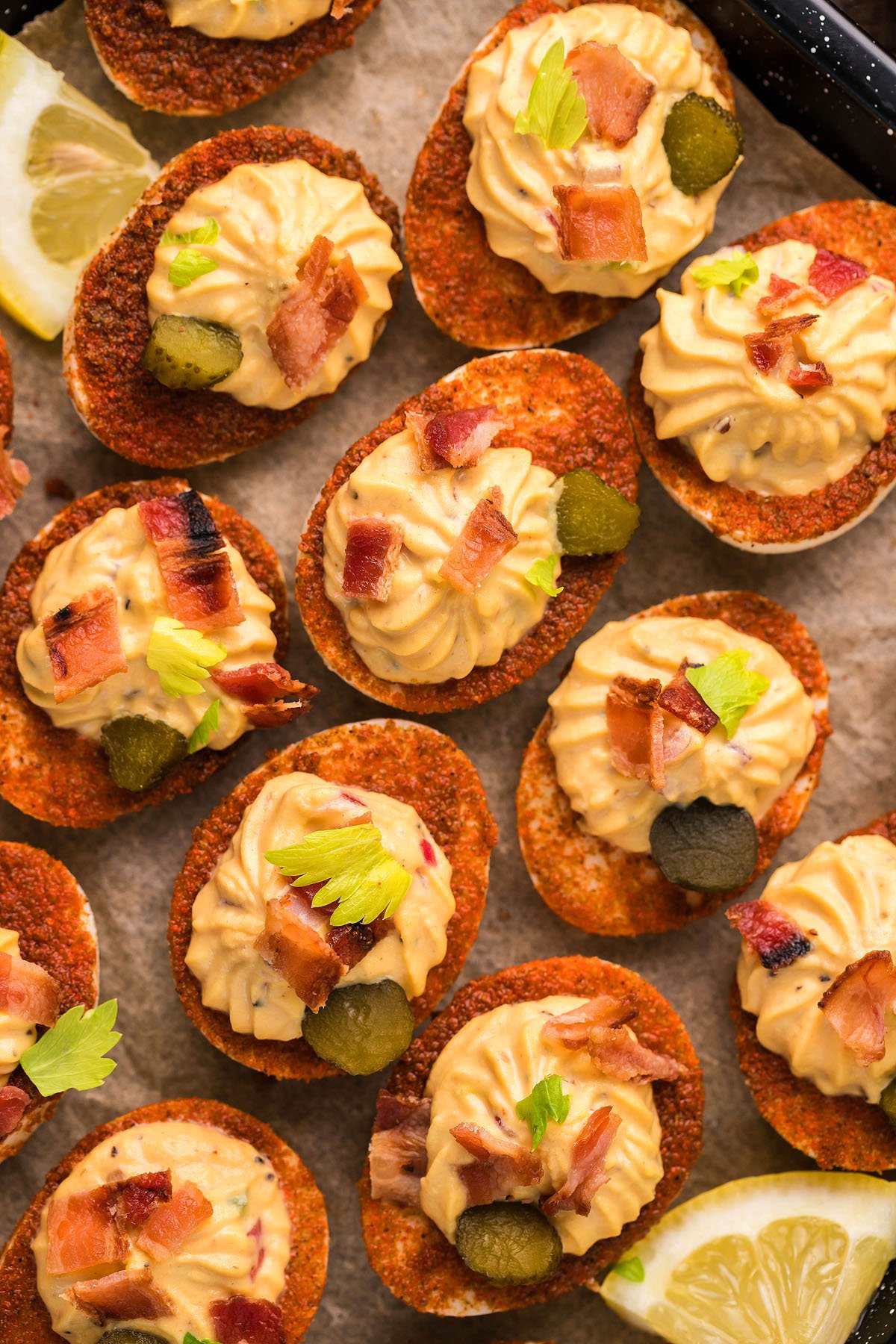 Potato chips topped with a loaded deviled eggs-inspired piped dip, bacon bits, pickles, and herbs, arranged on parchment with lemon wedges—a creative deviled egg idea for any gathering.