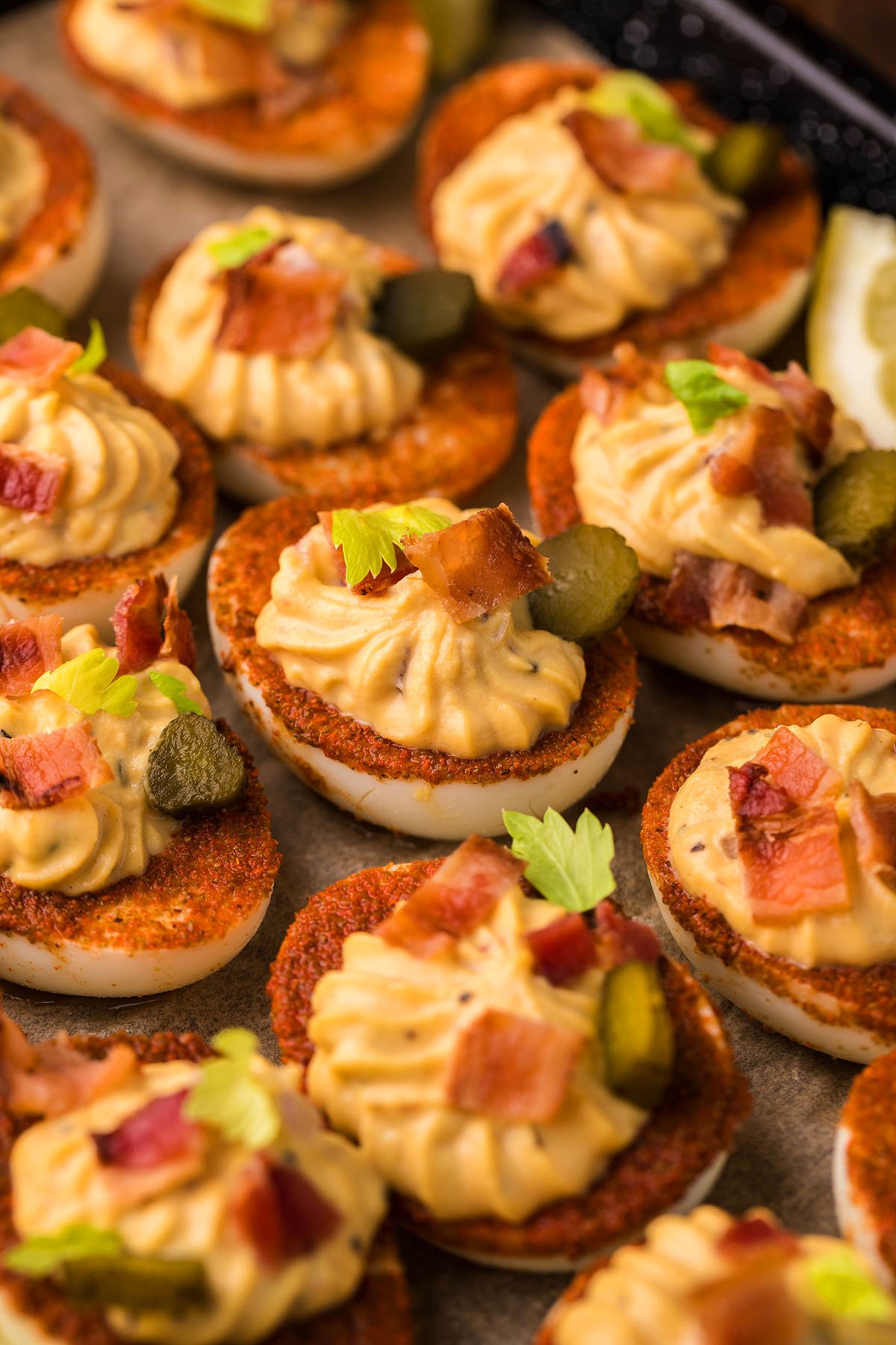 Bloody Mary Deviled Eggs topped with paprika, bacon, pickles, and herbs—a unique gourmet deviled egg idea arranged beautifully on a tray.