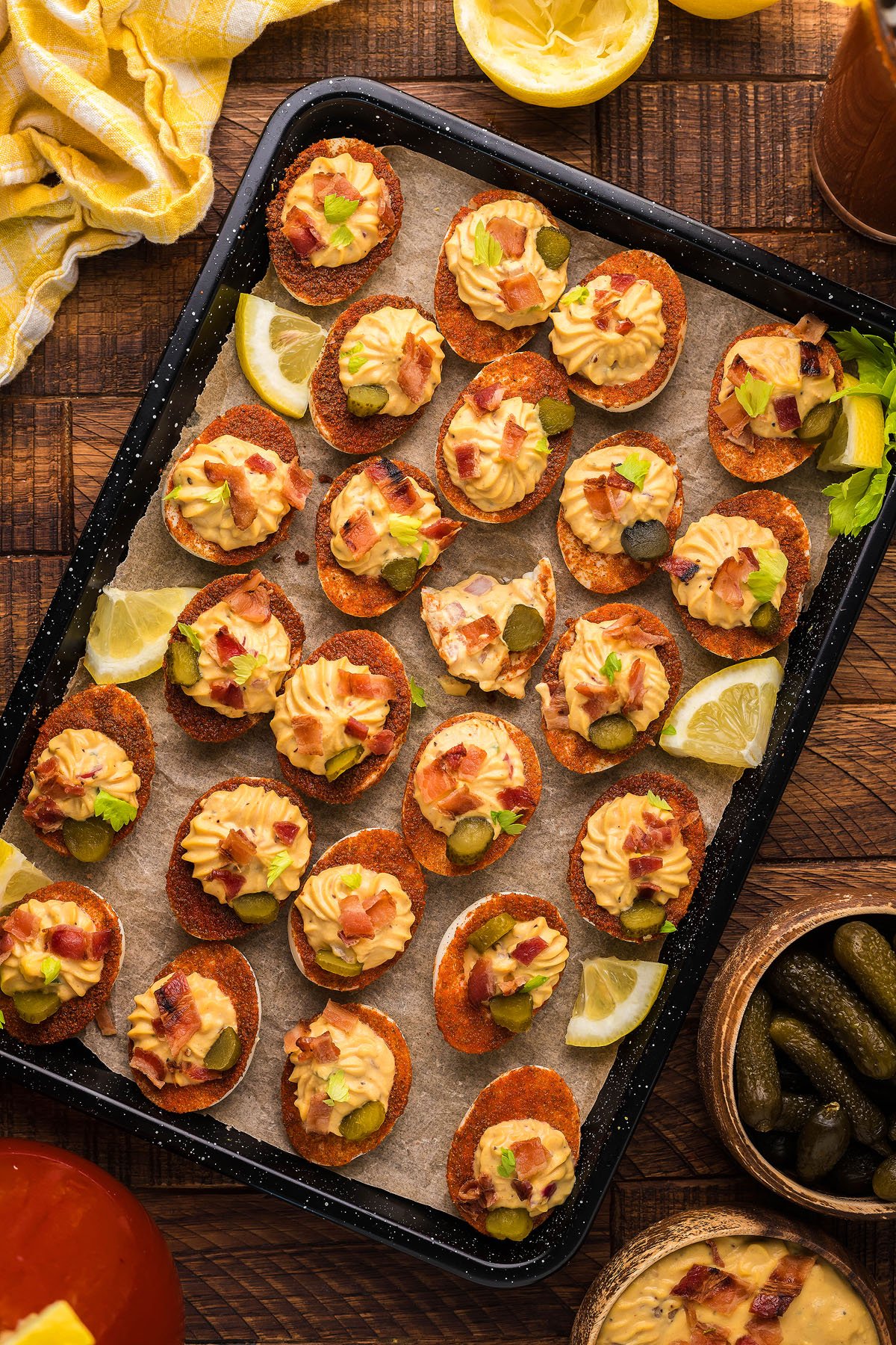 A tray of unique gourmet deviled eggs topped with creamy spread, pickles, bacon, and lemon wedges on the side—a creative deviled egg idea perfect for any gathering.