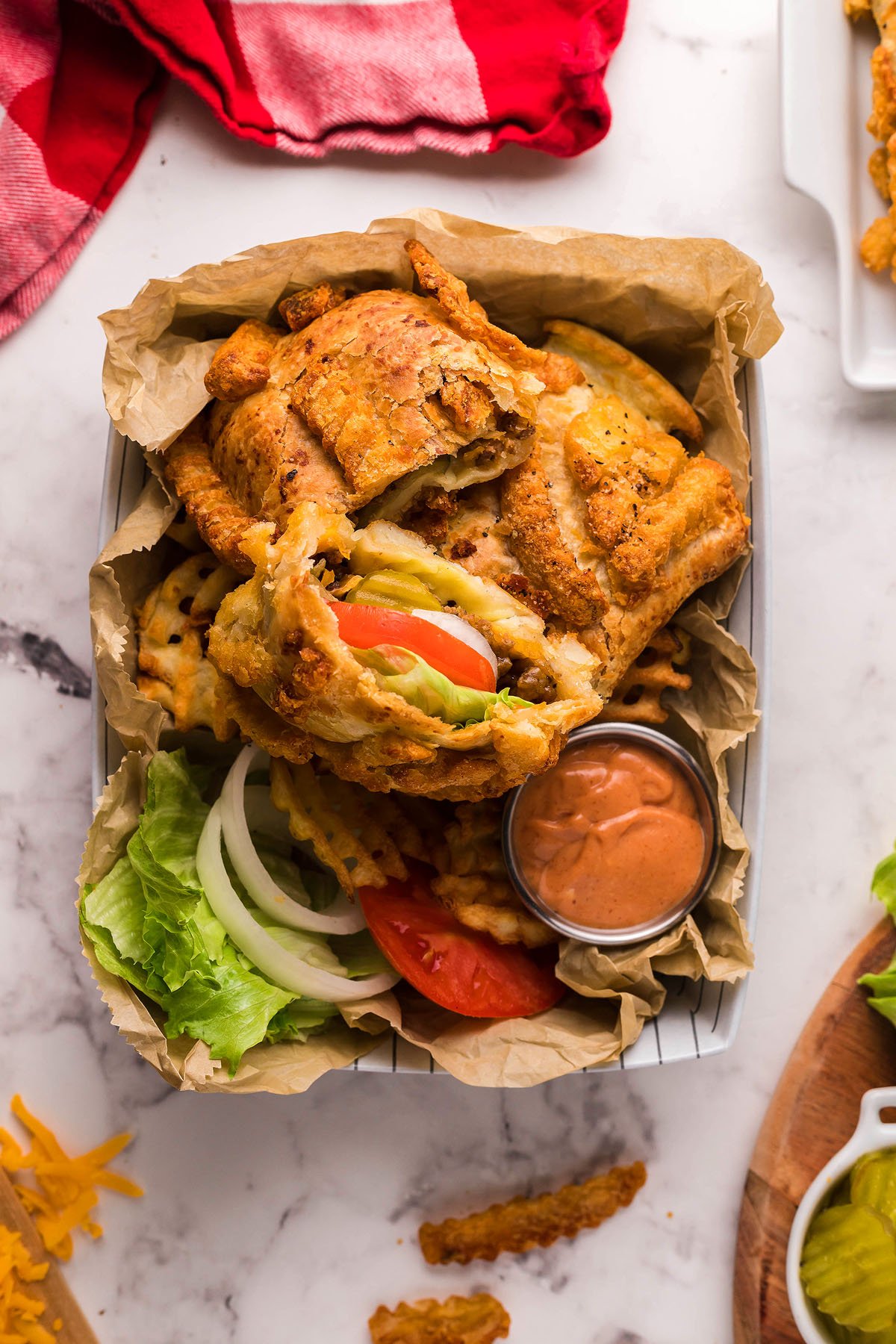 Fried chicken sandwich with lettuce, tomato, pickles, and sauce, served with waffle fries in a basket—try it with a French Fry Topping for an extra burst of flavor.