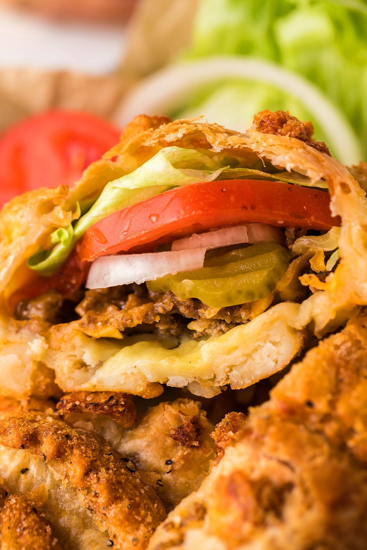Close-up of a fried puff pastry pocket burger cut open, showcasing layers of lettuce, tomato, onion, pickles, cheese, and beef.