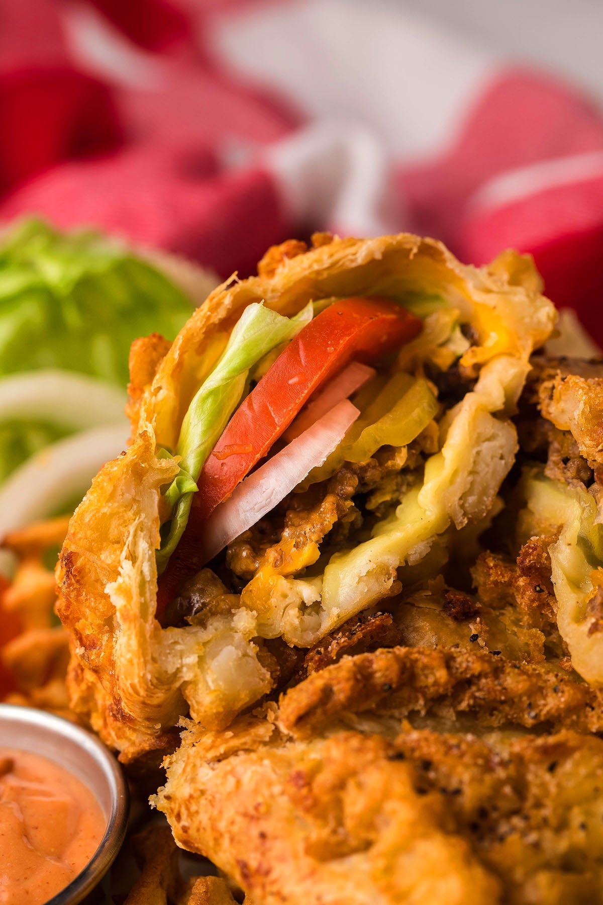 Close-up of a cheeseburger egg roll cut open, showing lettuce, tomato, onions, cheese, and ground beef inside—like a cheesy Puff pastry pocket burger in every bite.