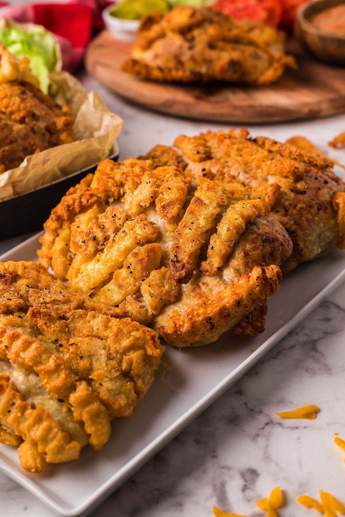 Golden, crispy fried chicken fillets on a white rectangular plate, paired with toppings and inspired by the bold flavors of burger empanada in the background.