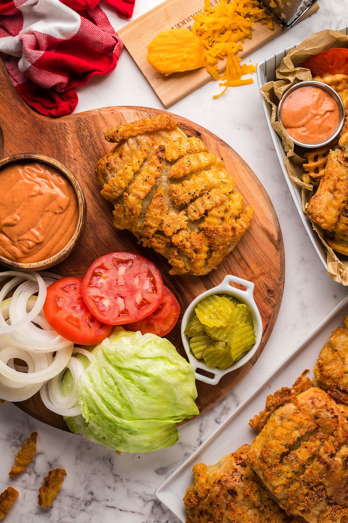 Crispy fried chicken, sliced tomatoes, onions, lettuce, pickles, and sauce on a wooden board—perfect as a French fry topping or paired with cheeseburger hand pies.