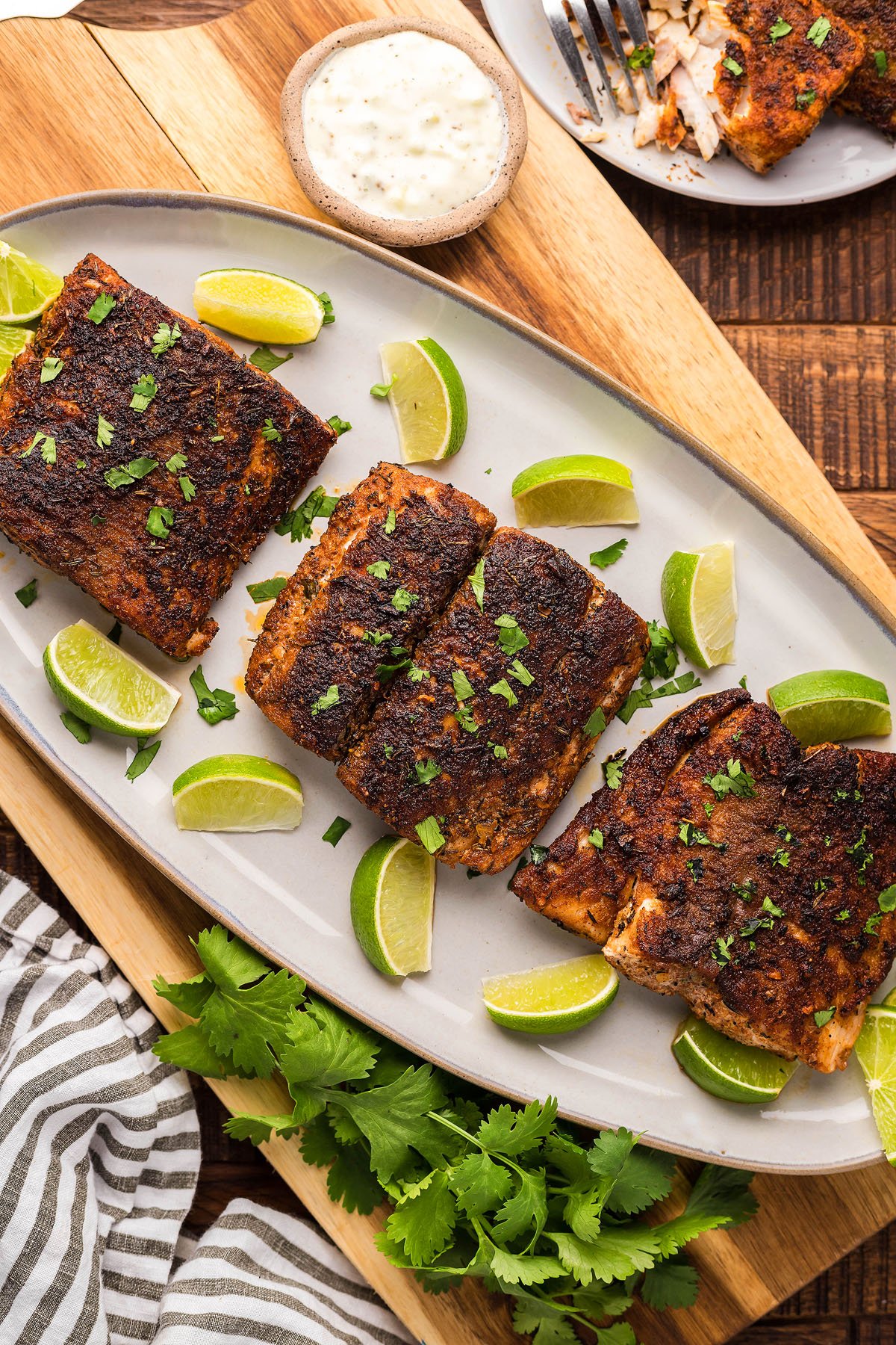 Blackened Mahi Mahi fillets on a plate with lime wedges, fresh cilantro, and a small bowl of white sauce, made with Homemade Seasoning for bold Cajun flavor.